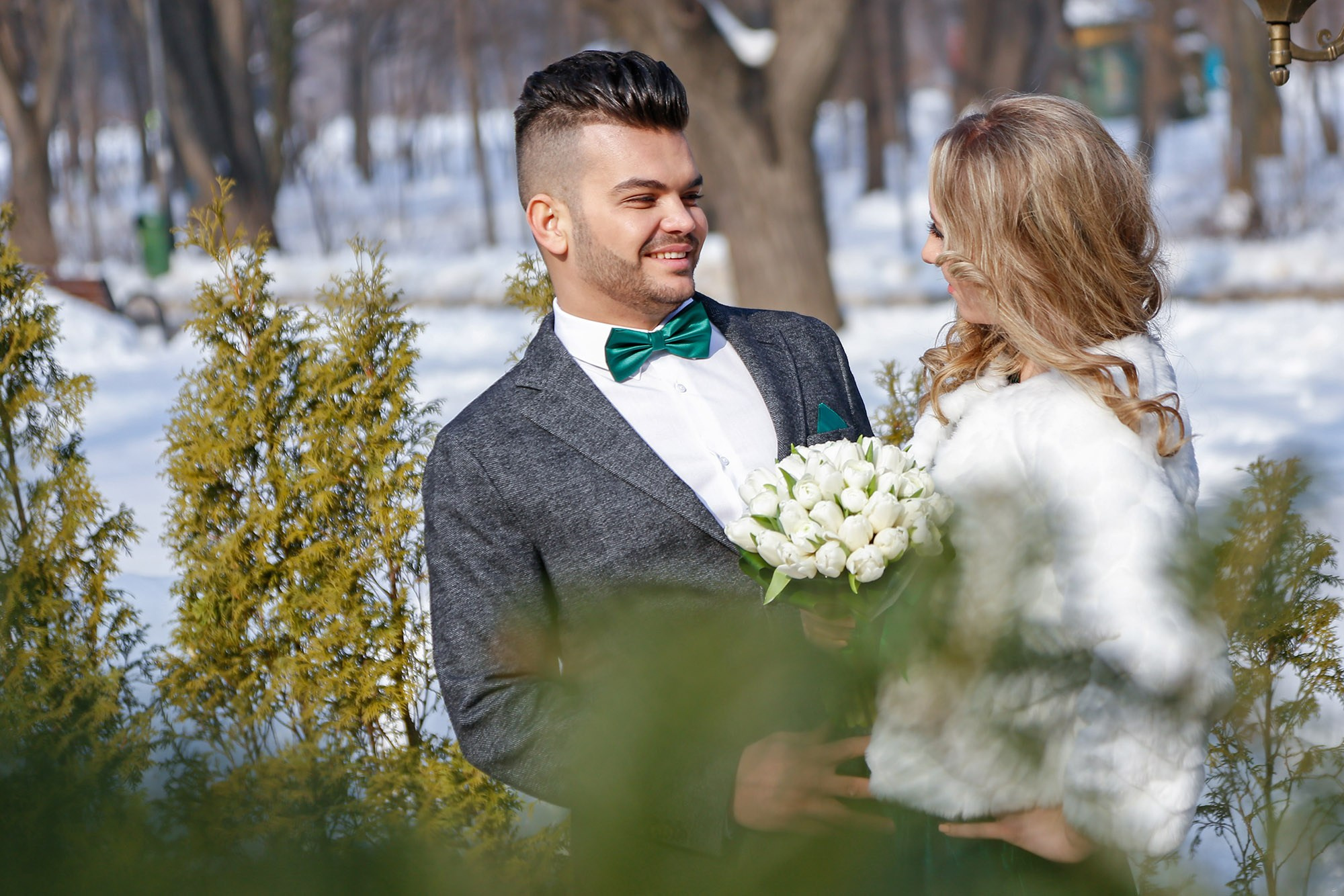 Romantic portrait of the newlyweds holding each other close amidst frozen nature, highlighting the contrast between the white jacket and elegant suit.