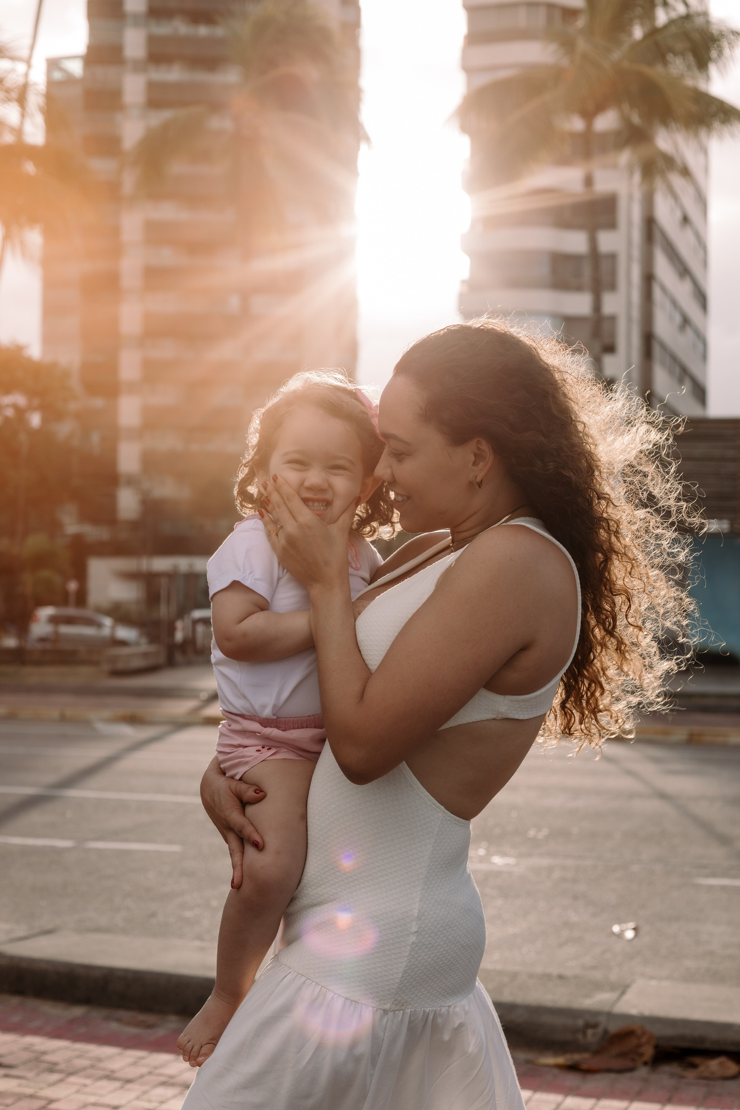 Foto mãe e filha ao por do sol com prédios ao fundo