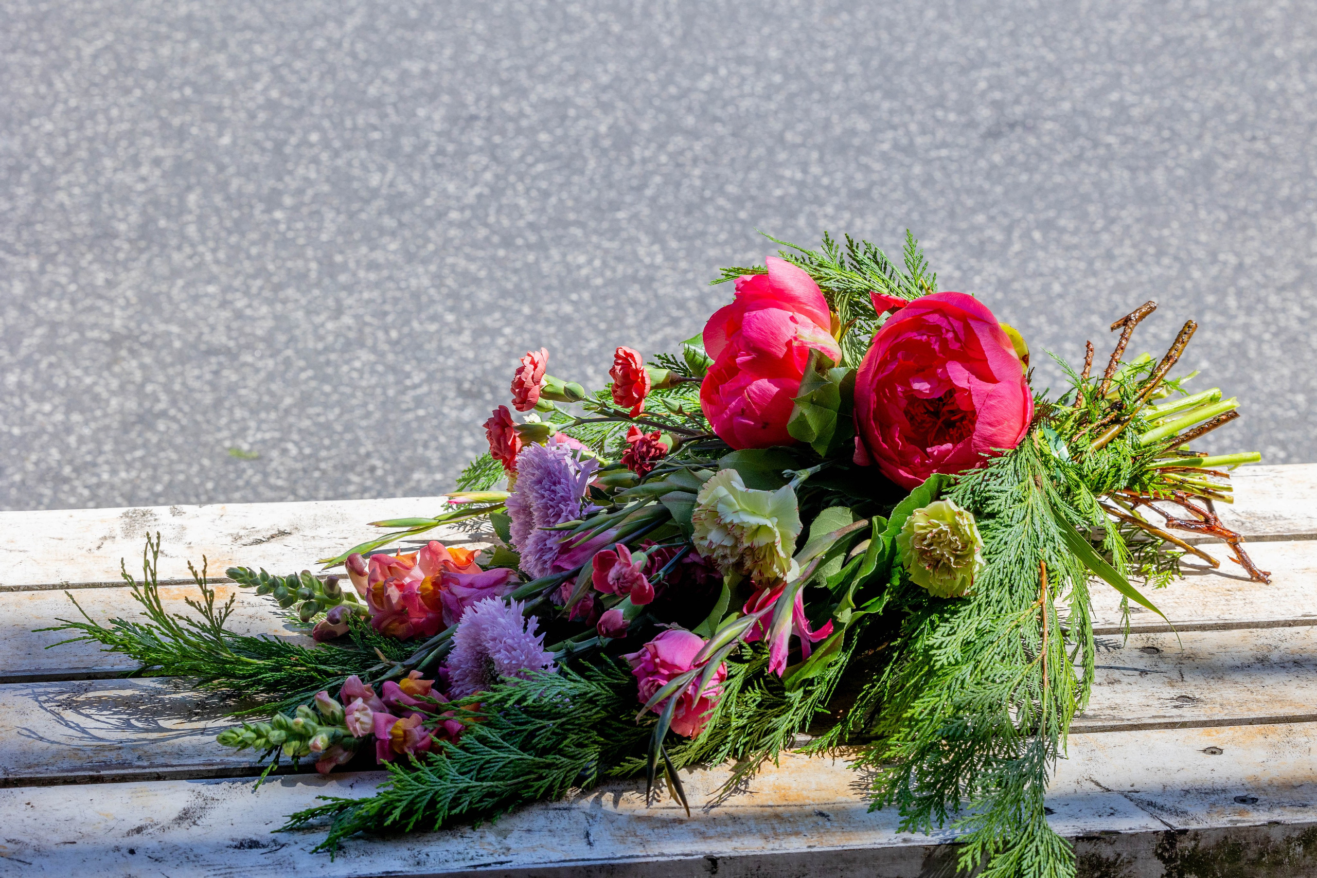 En bølge af lyserød elegance: Bårebuket med spredt arrangementDenne bårebuket er et unikt og smukt minde. Blomsterne er arrangeret på en måde, så de ligger elegant udstrakt, hvilket skaber en følelse af luftighed og fred.  Hver blomst får lov til at skinne for sig selv, fremhævet af det strategisk indflettede, blandede grønt.