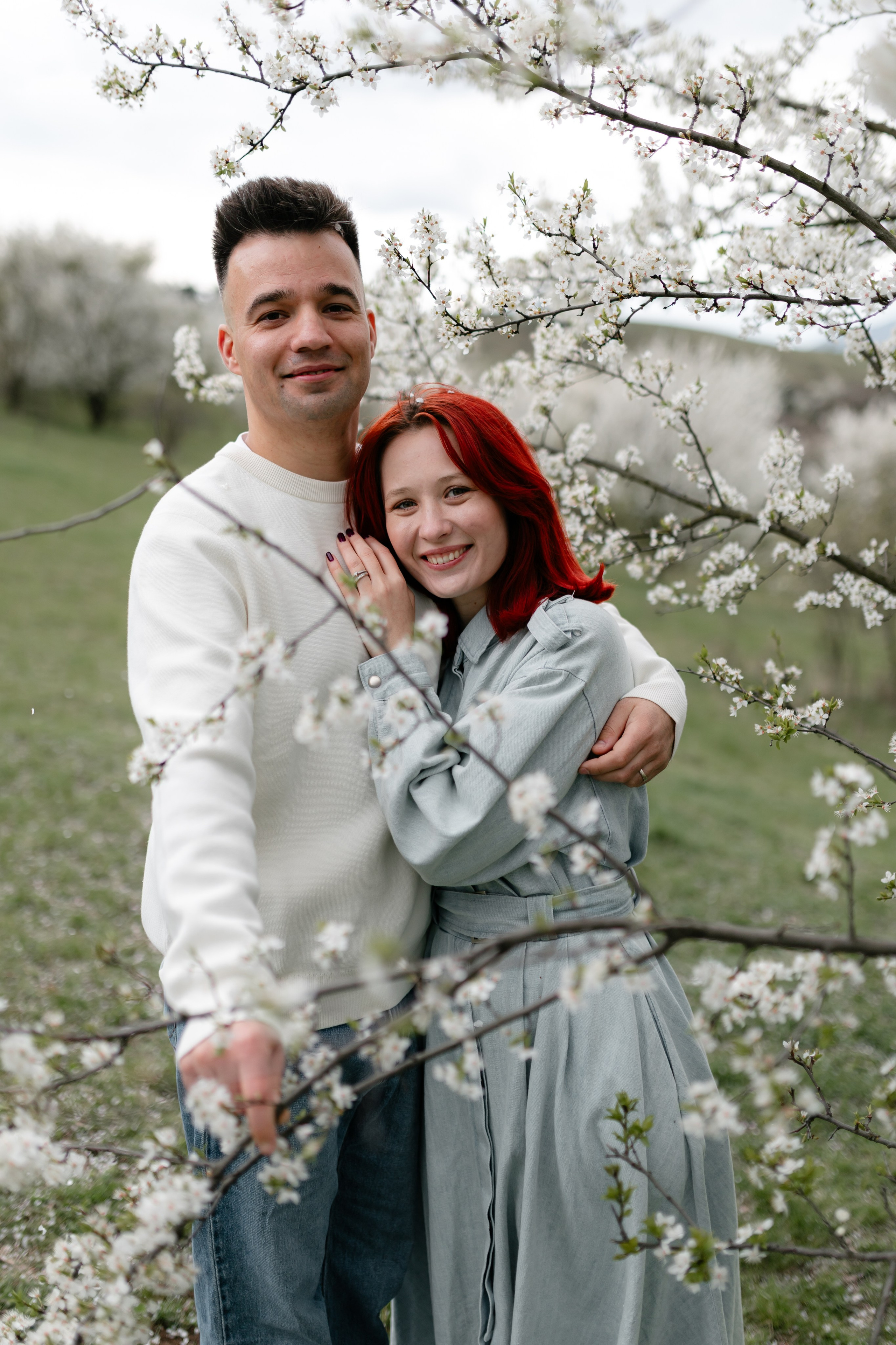 A couple surrounded by spring blossoms, looking at the camera.