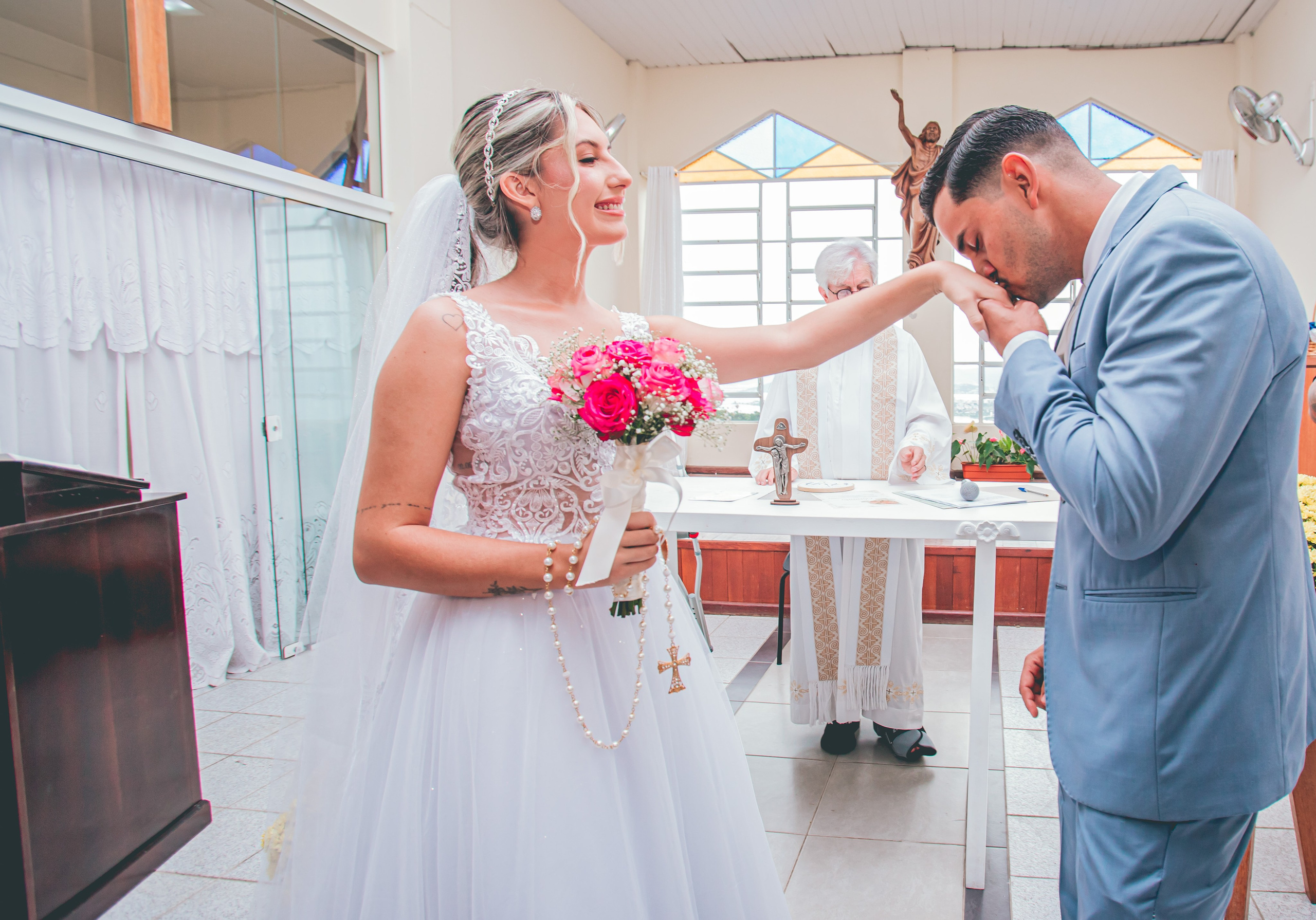 Foto de noiva recebendo beijo na mão do noivo na igreja