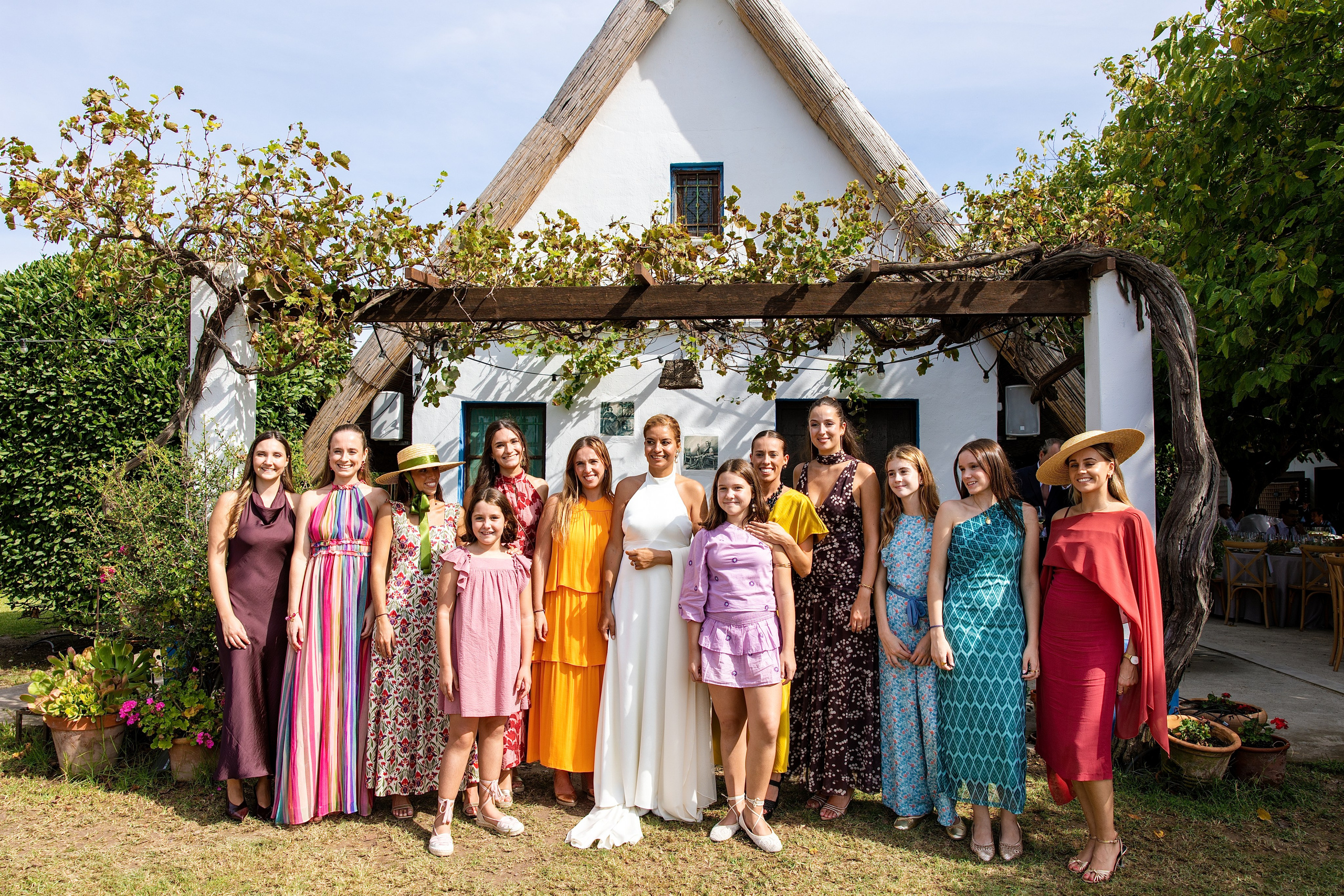 Foto de grupo de invitados con vestidos de colores delante de la barraca, boda en La Baraca del Palmar