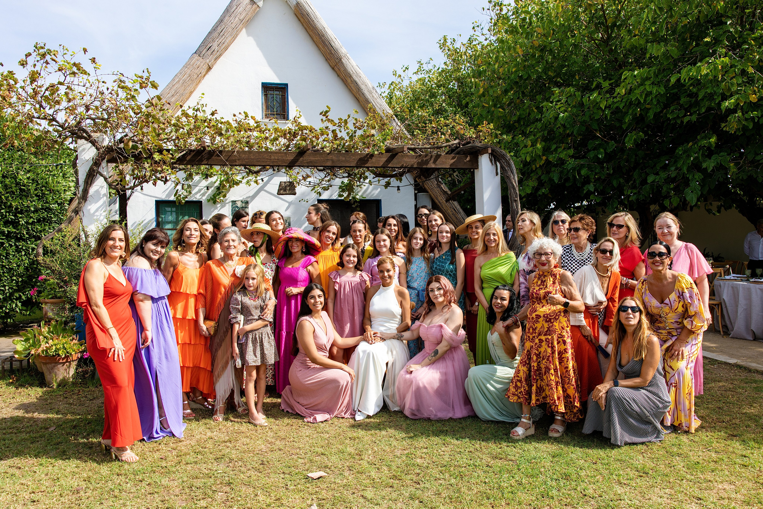 Foto de grupo de invitados con vestidos de colores delante de la barraca, boda en La Baraca del Palmar