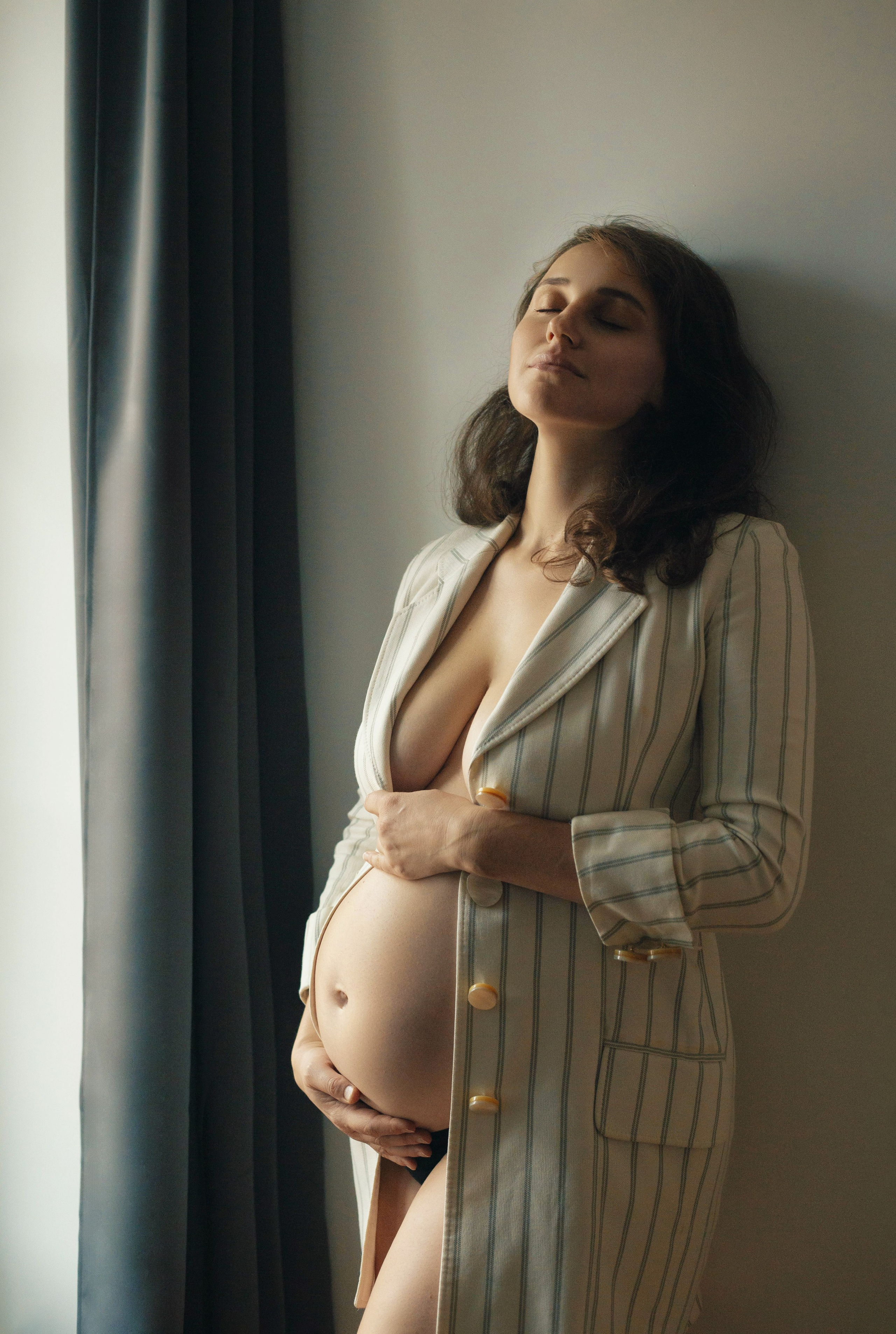 Séance photo grossesse naturelle près de la fenêtre, femme enceinte en chemise blanche