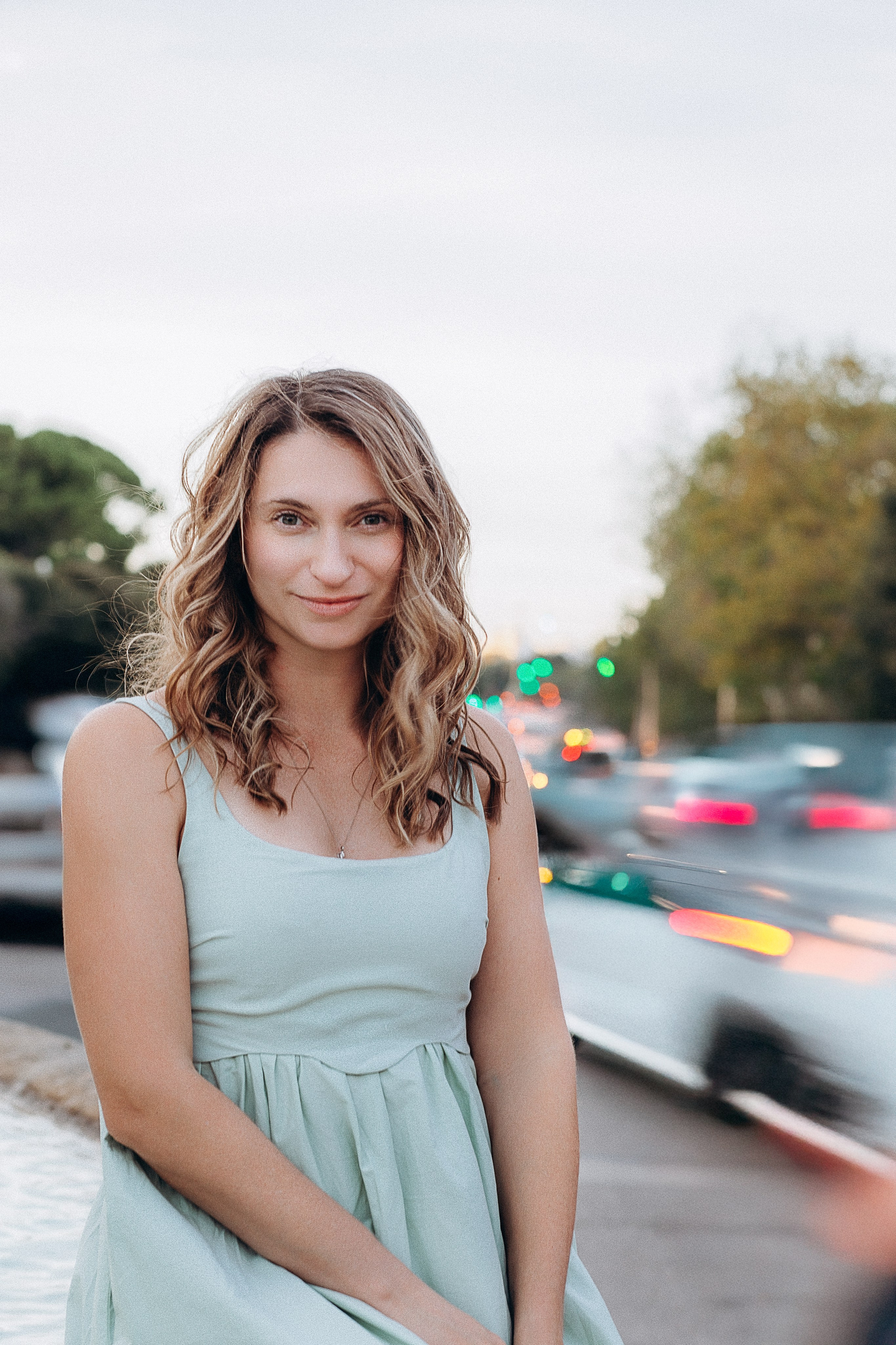 Естественный женский портрет, снятый в Валенсии, Испания, с улыбающейся женщиной с волнистыми волосами в нежно-сером платье на городской улице во время золотого часа — идеально подойдёт тем, кто ищет расслабленные и аутентичные женские фотосессии в Валенсии и по всей Испании.