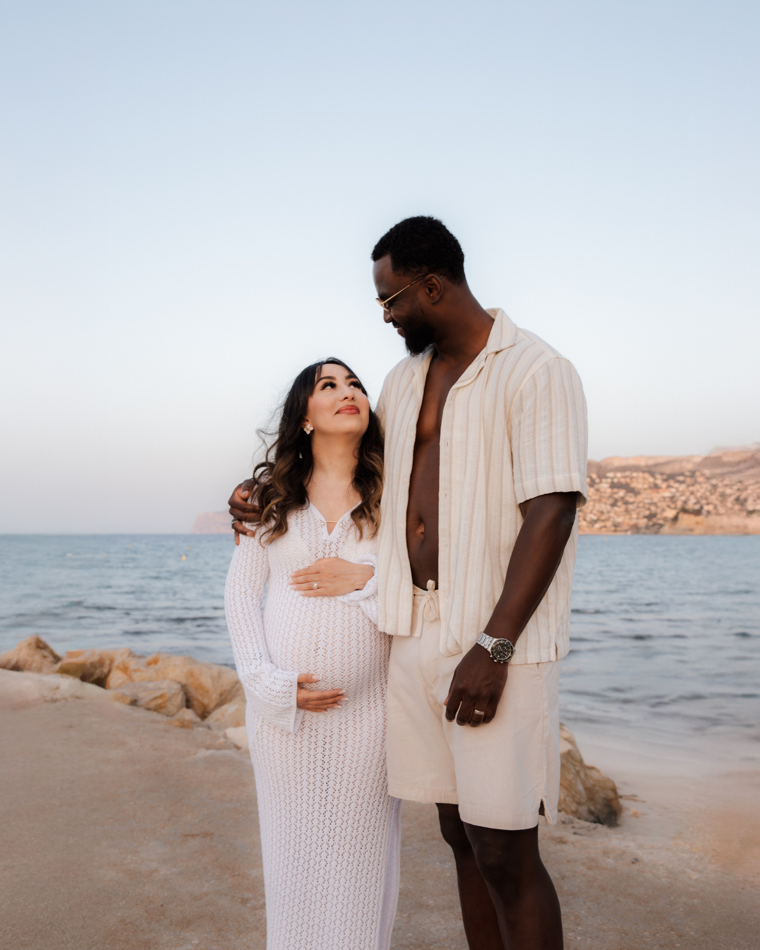 Sesión romántica de maternidad en Altea, España — pareja enamorada junto al mar Mediterráneo, la futura madre sosteniendo su vientre mientras mira a los ojos de su pareja. Un momento precioso en la Costa Blanca.