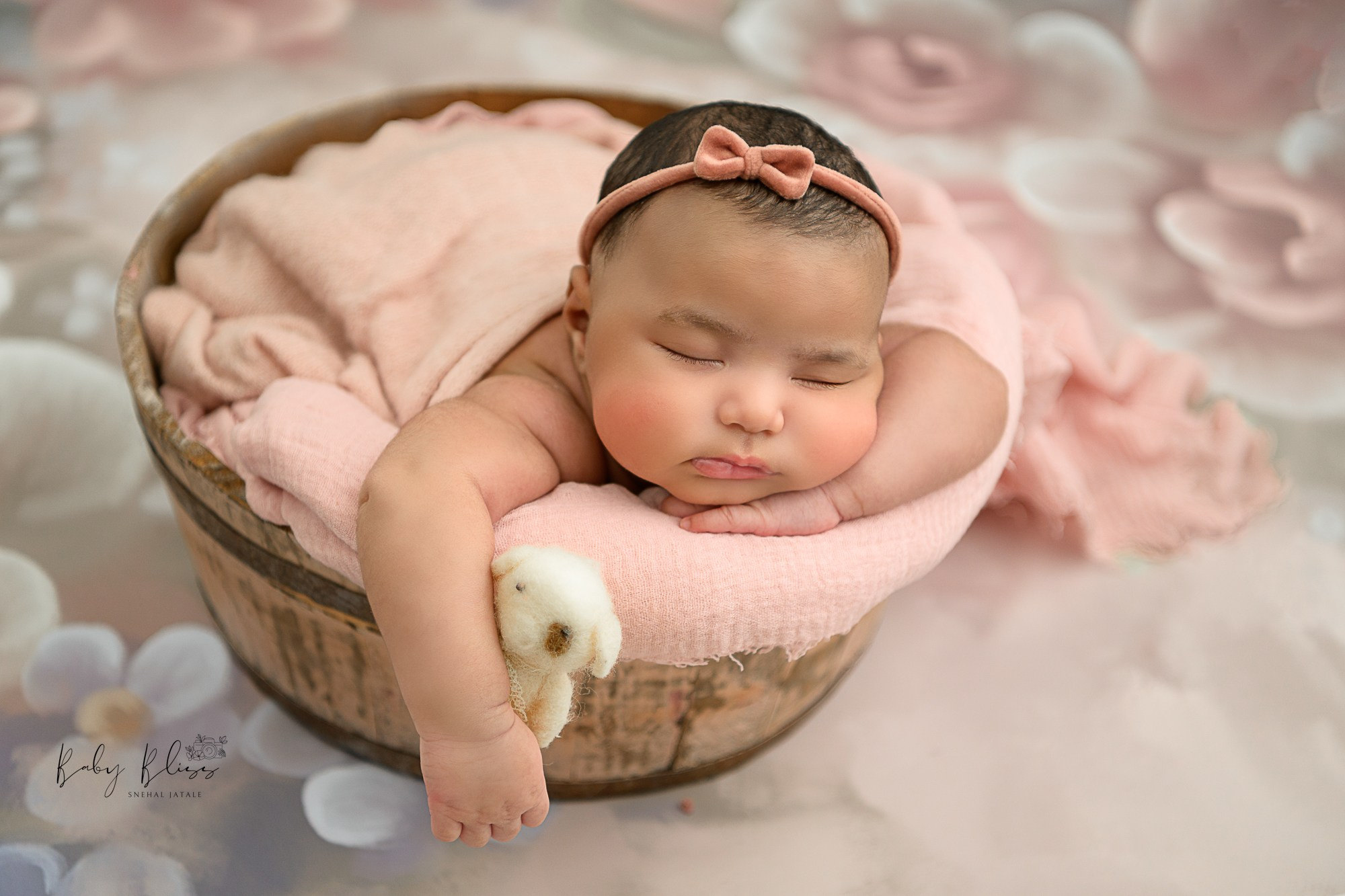 chubby newborn baby girl in dusky pink wrap holding a tiny toy in a basket.