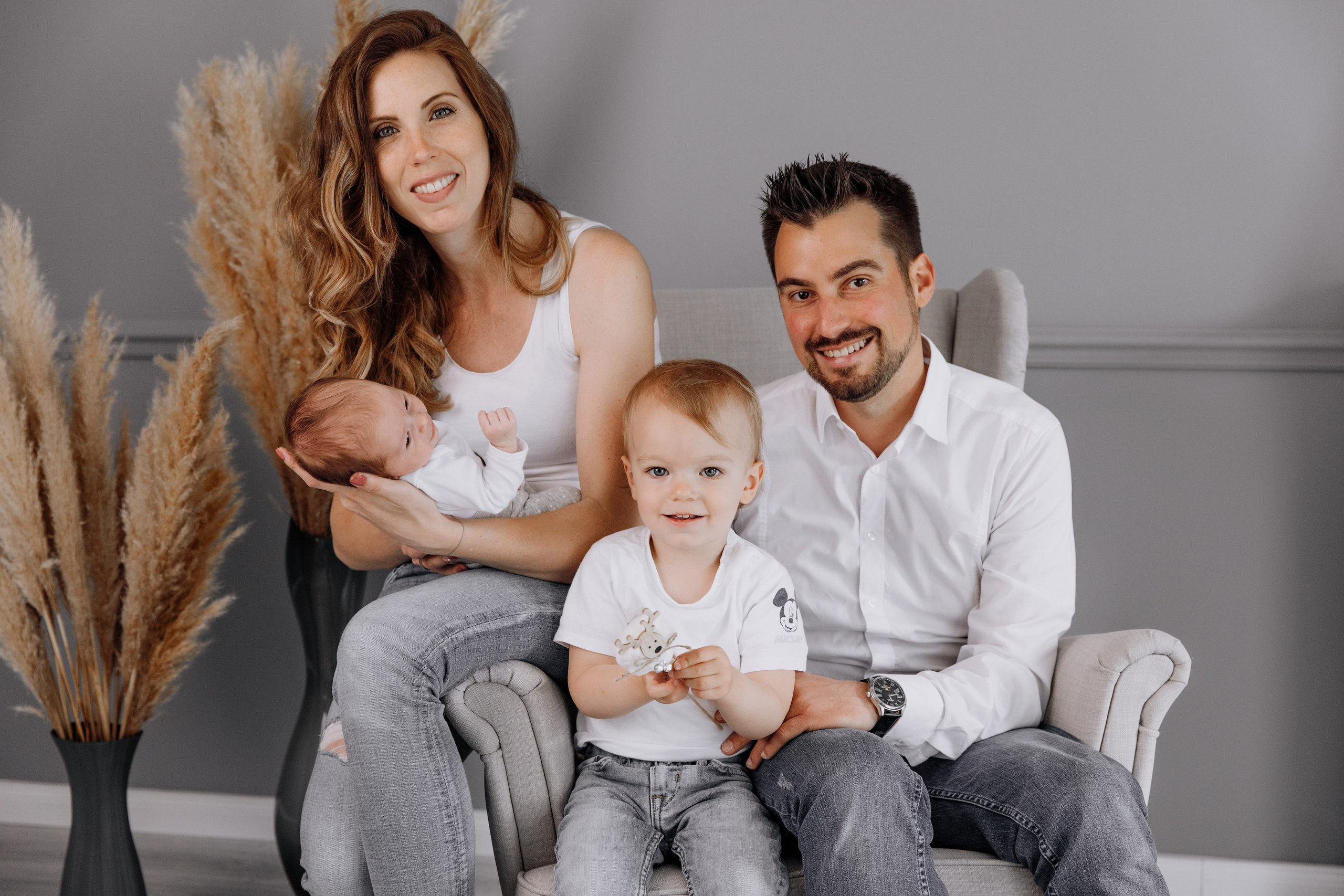 Die ganze Familie sitzt gemeinsam auf dem Sessel, während die Mutter das Baby liebevoll im Arm hält.