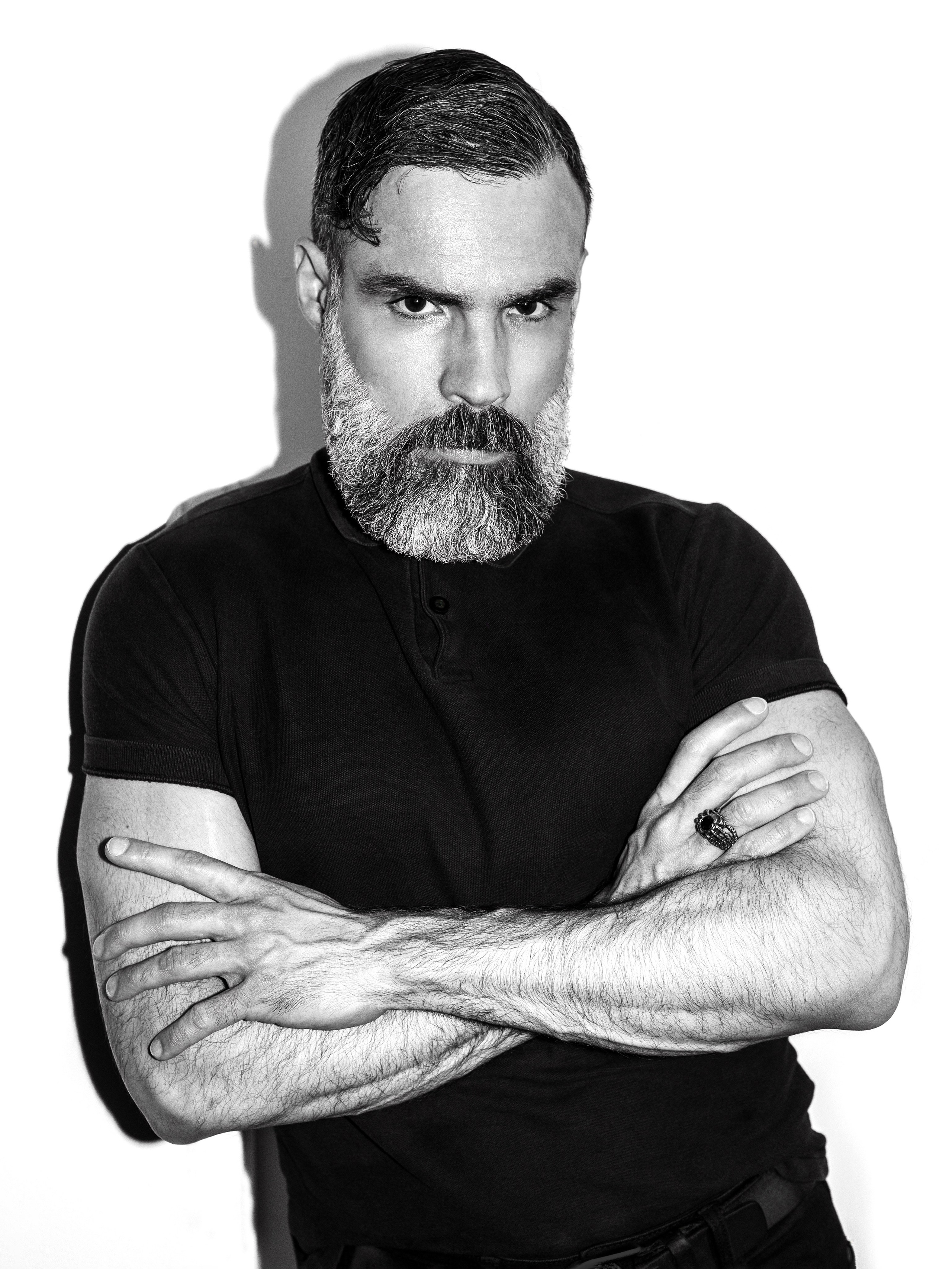 Черно-белый снимок,  красивый мужчина с бородой стоит, скрестив руки на груди