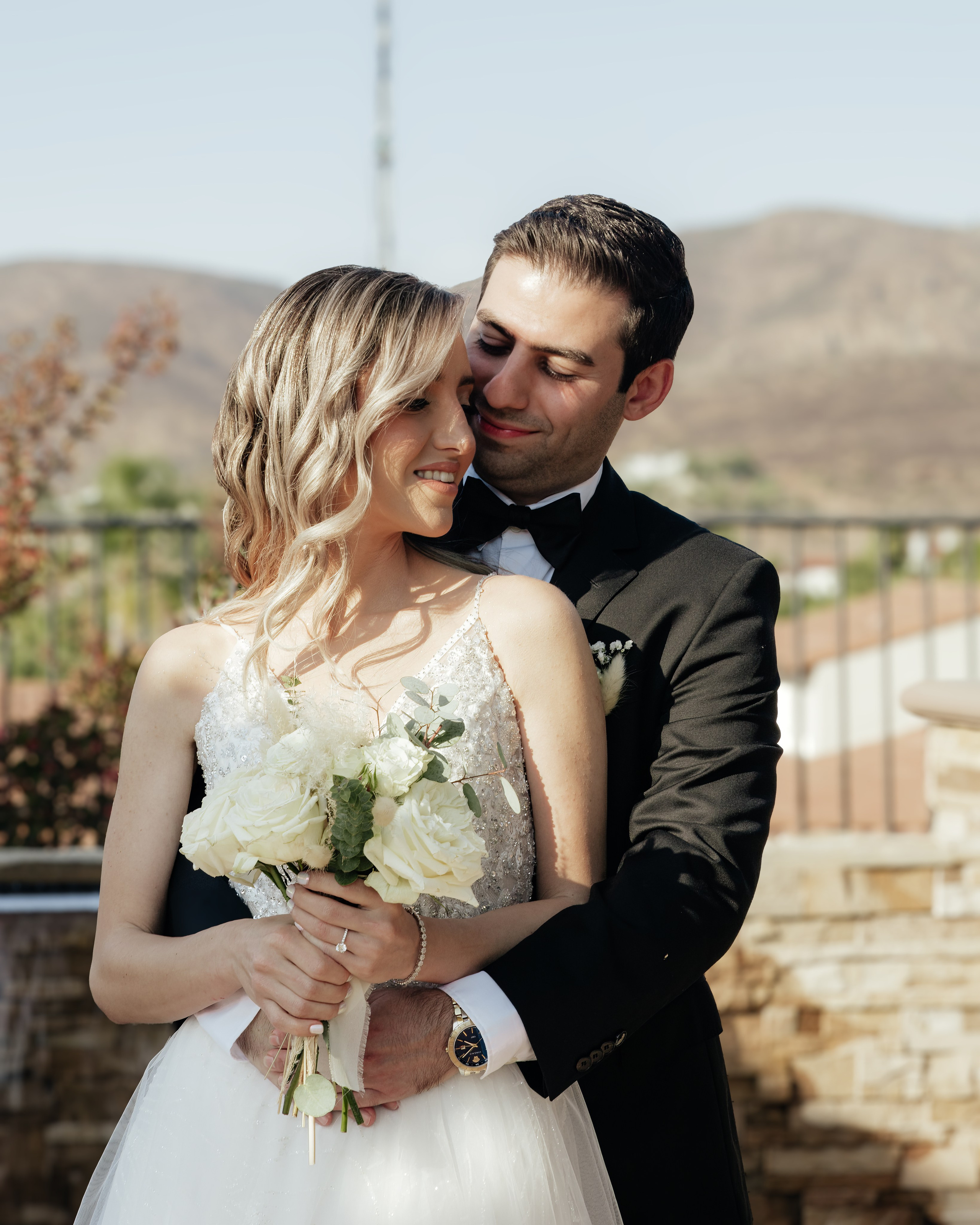 Groom hugging bride from behind in a natural outdoor setting during wedding session