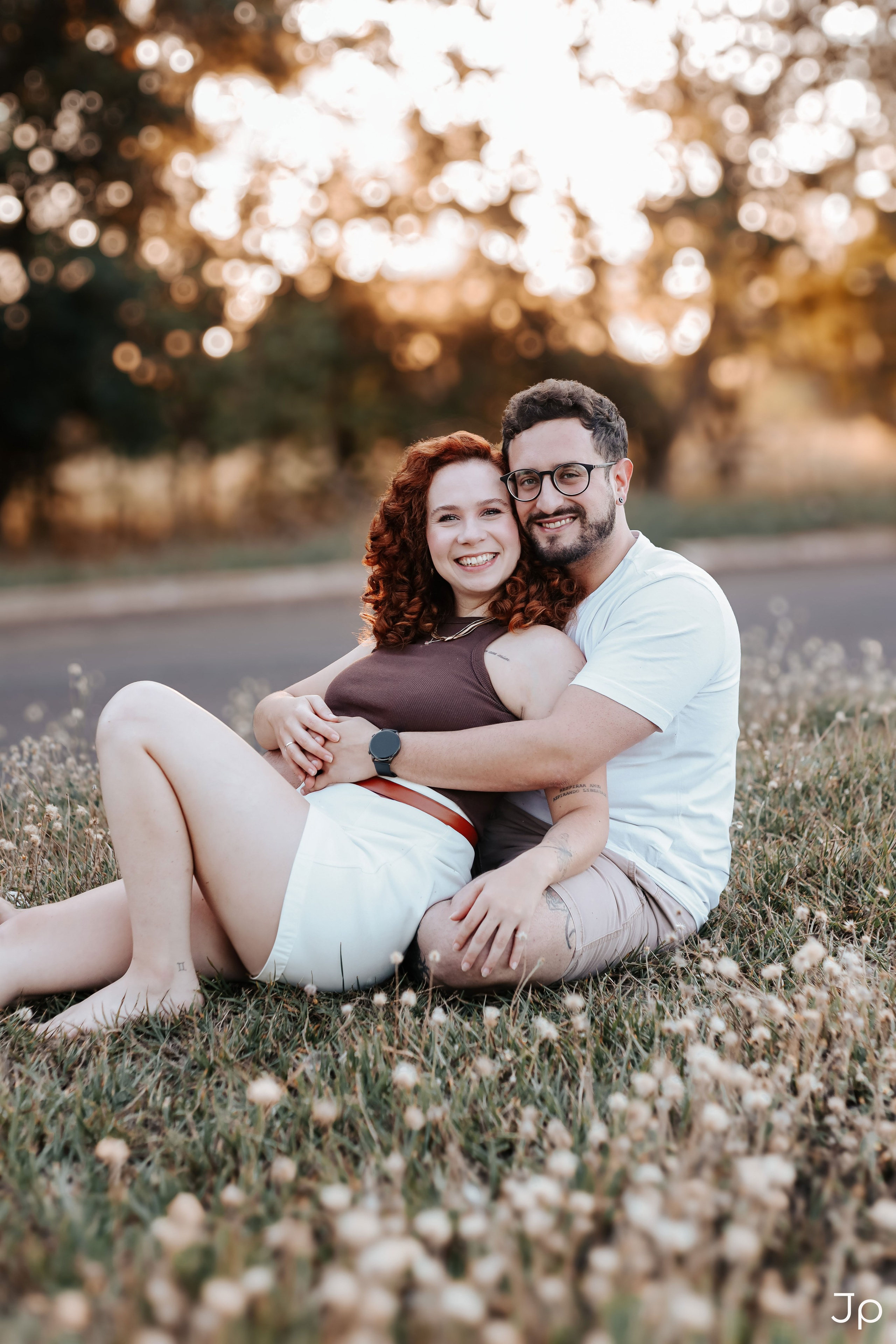 Casal sentado na grama, abraçados e sorrindo.