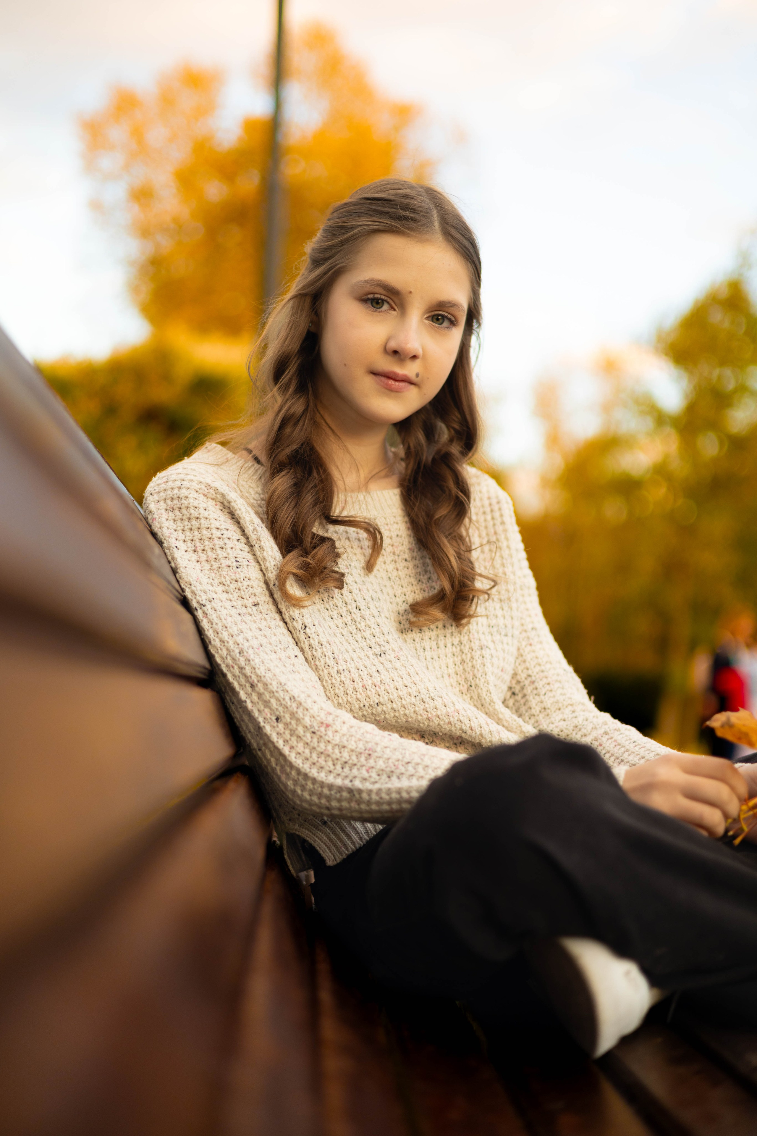 Девушка сидит на скамейке, вокруг опавшие листья — осенняя фотосессия.