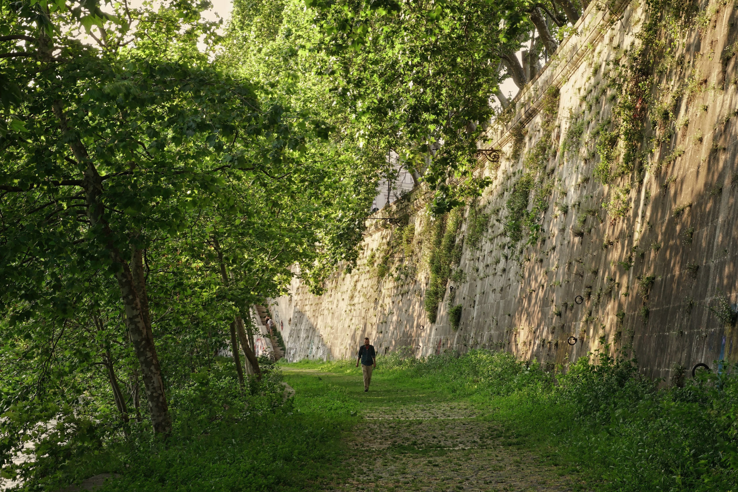 Photography of Italy – Banks of the Tiber River in Rome in summer with a solitary figure walking along the river, photographed as part of a photography book about Rome.