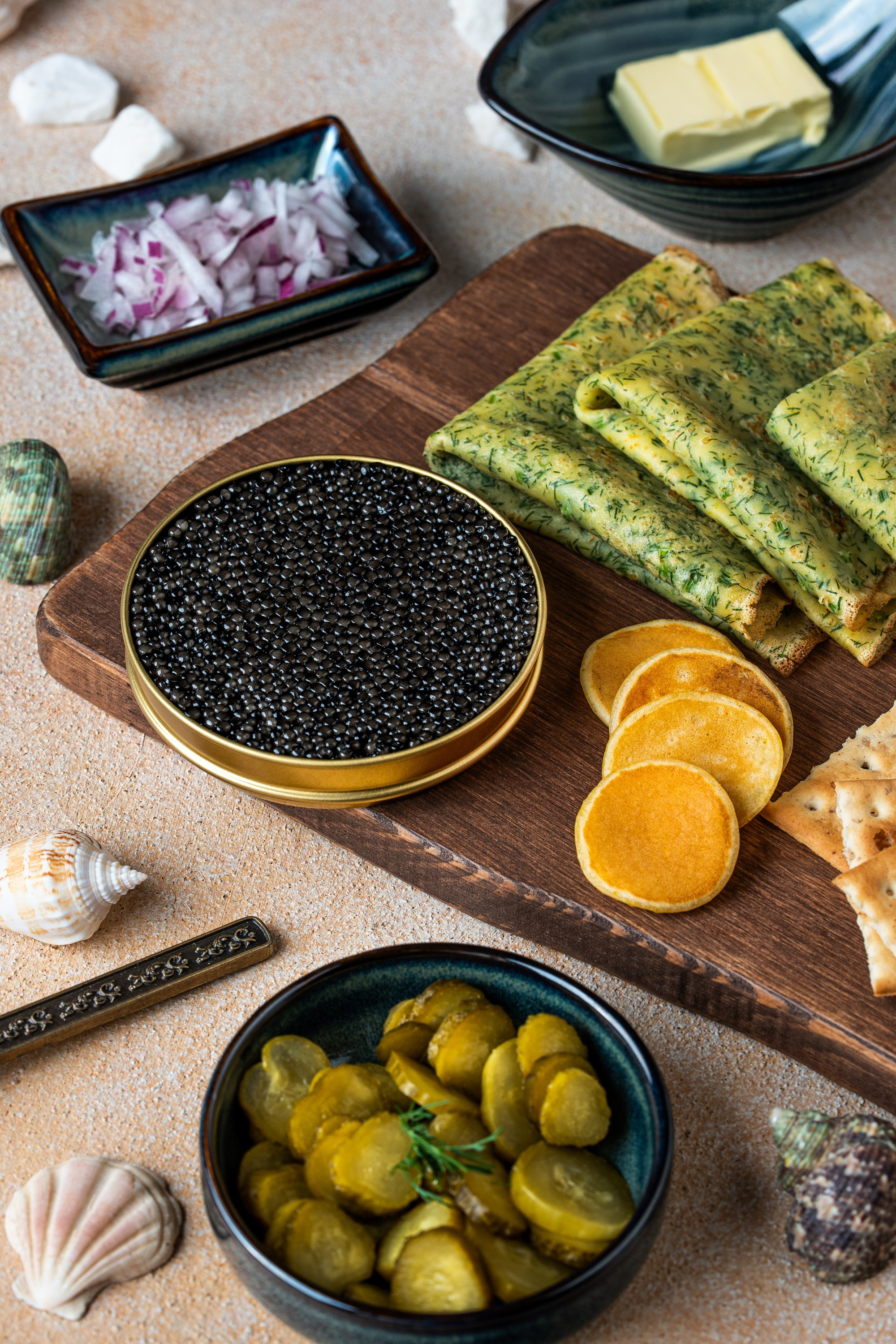 Qızılı qutuda qara kürü, blinçik, duzlu xiyar və dəniz qabıqları ilə süfrə düzümü