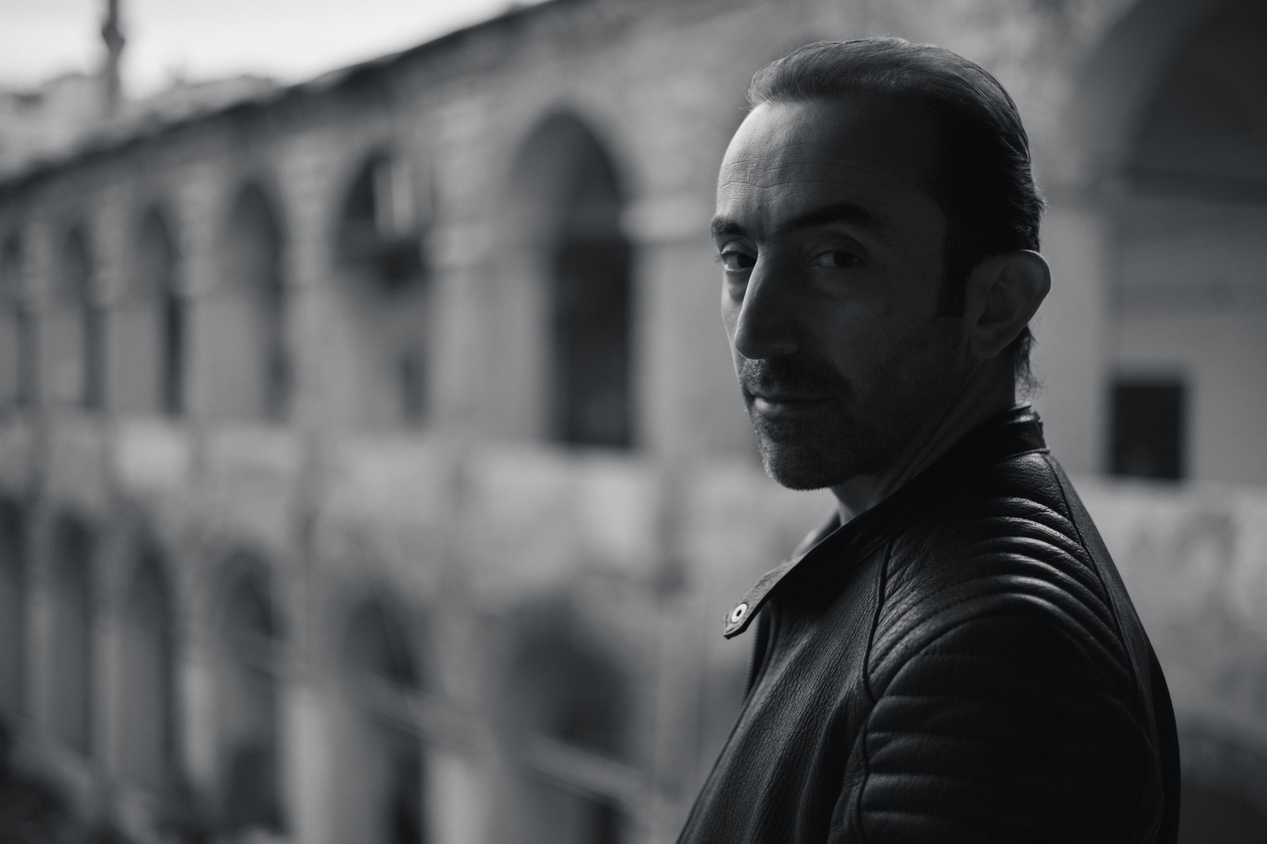 Мужчина в кожаной куртке смотрит в камеру в исторической аркаде Стамбула