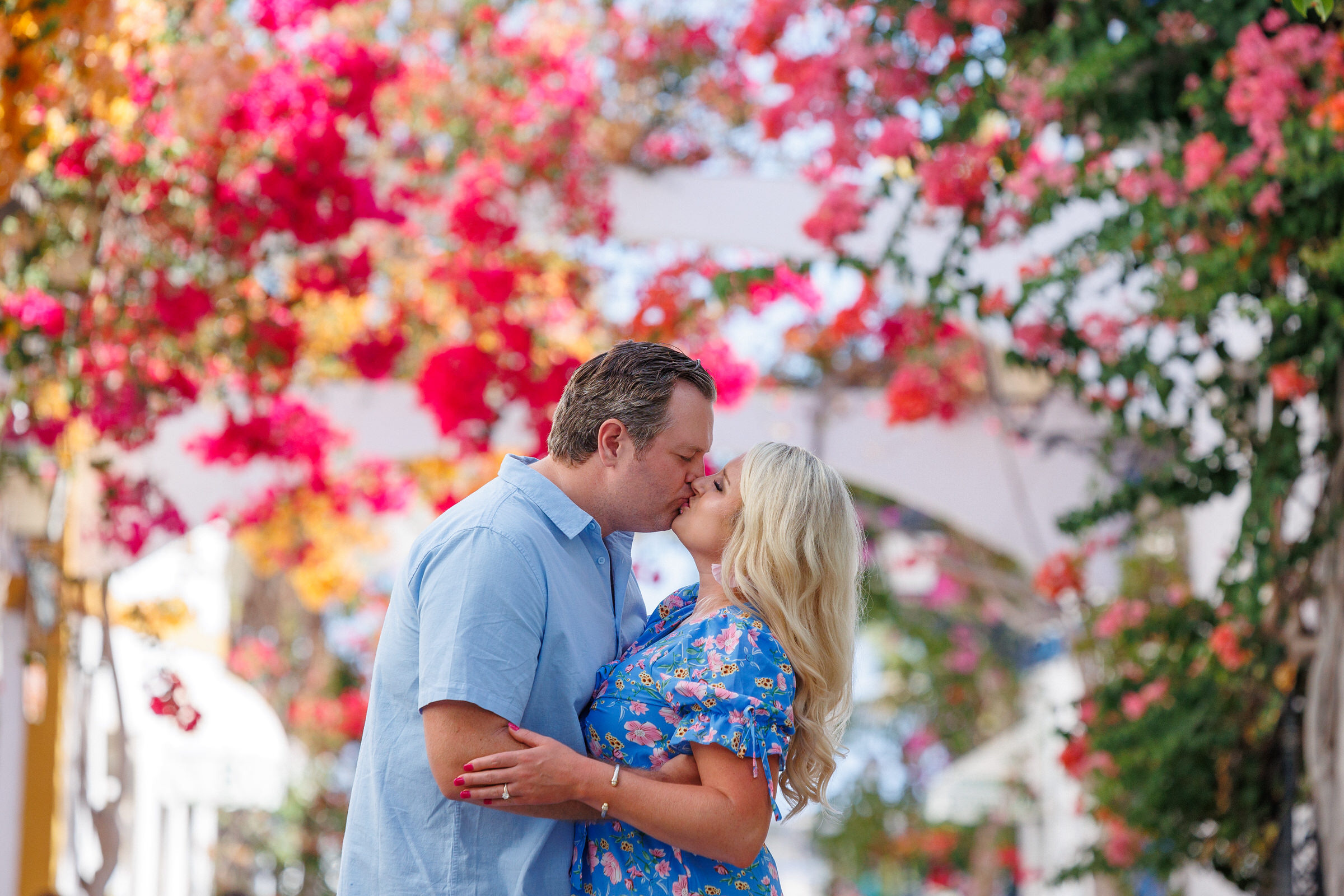 Captured against the picturesque backdrop of Gran Canaria's stunning landscapes, this enchanting photograph features an engaged couple sharing a tender moment amidst a breathtaking display of vibrant bougainvillea flowers. As the sun sets, casting a warm glow over the scene, the couple's love is beautifully accentuated by the riot of colors surrounding them. The skilled photographer skillfully frames the lovers, immortalizing their affectionate kiss and creating a timeless memory of romance and natural beauty on the captivating island of Gran Canaria