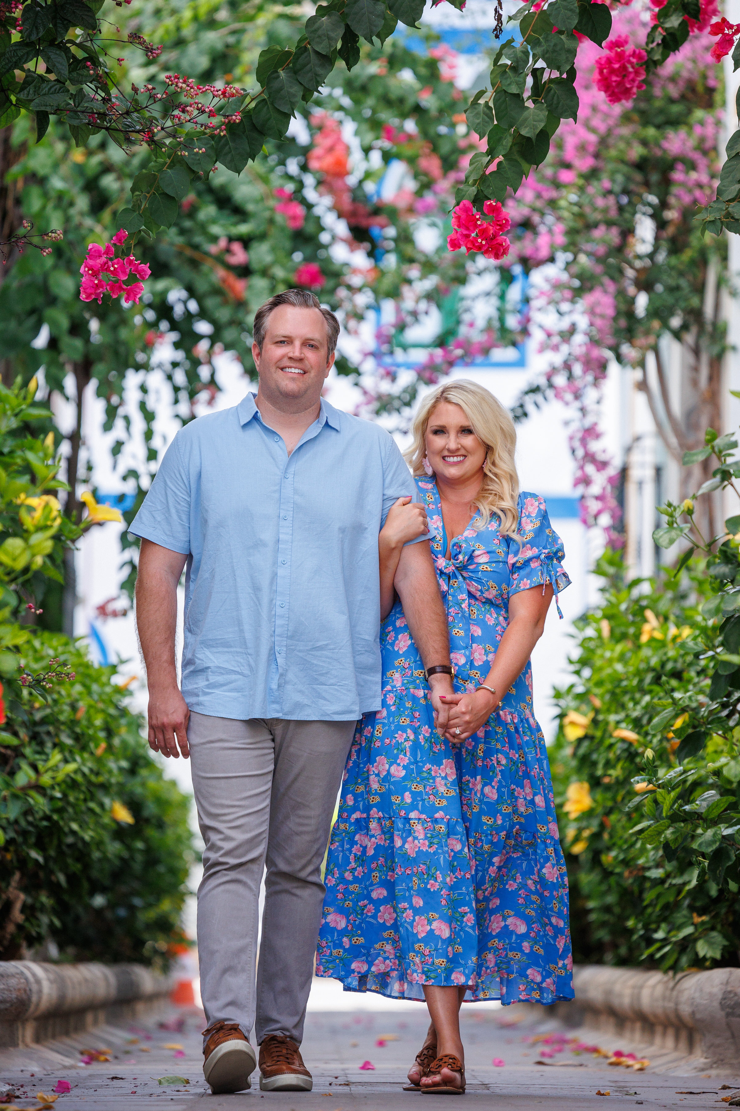 Puerto De Mogan Photoshoot A couple walking down a pathway with flowers in the background.