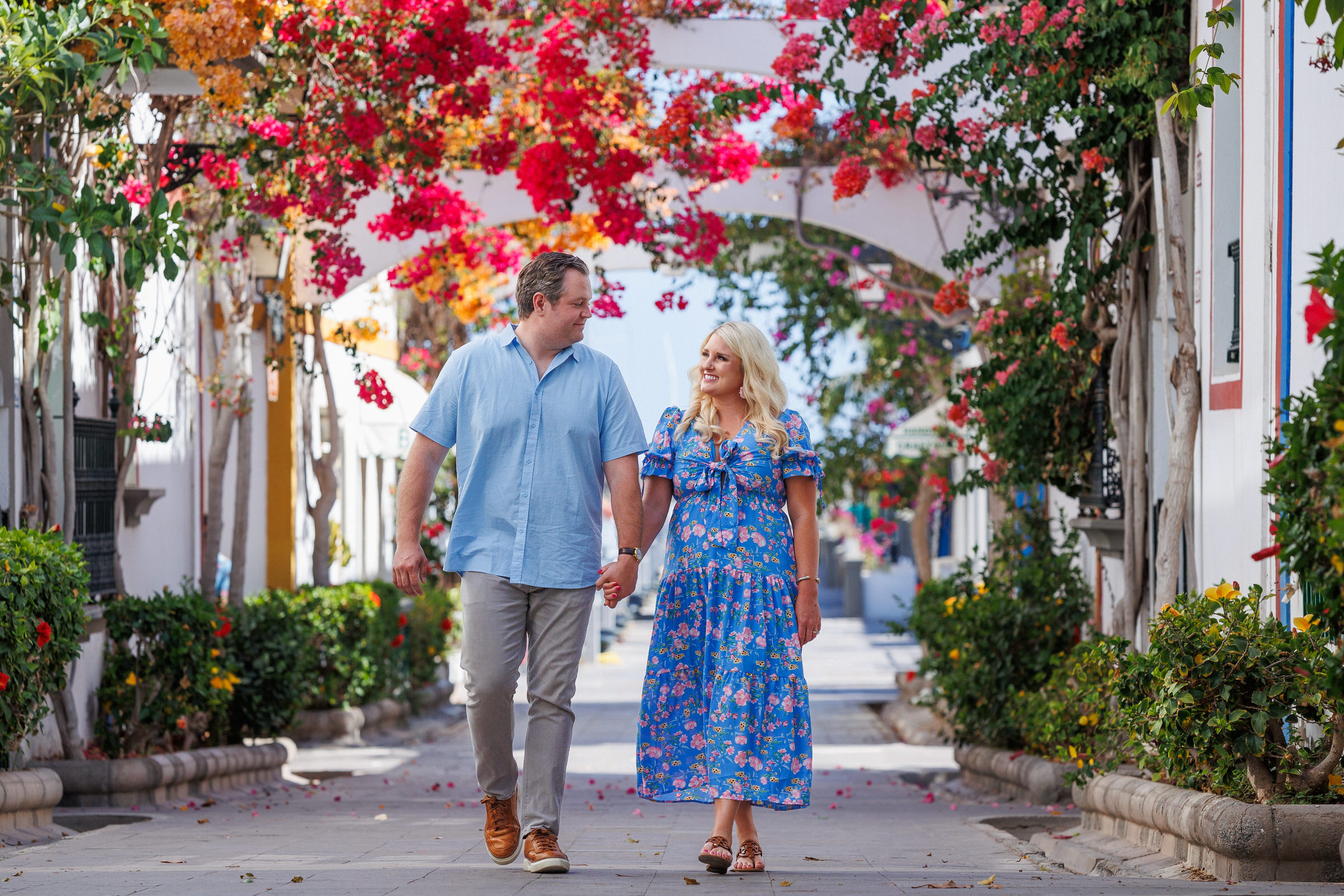A couple walking down a narrow alley with flowers in the background.