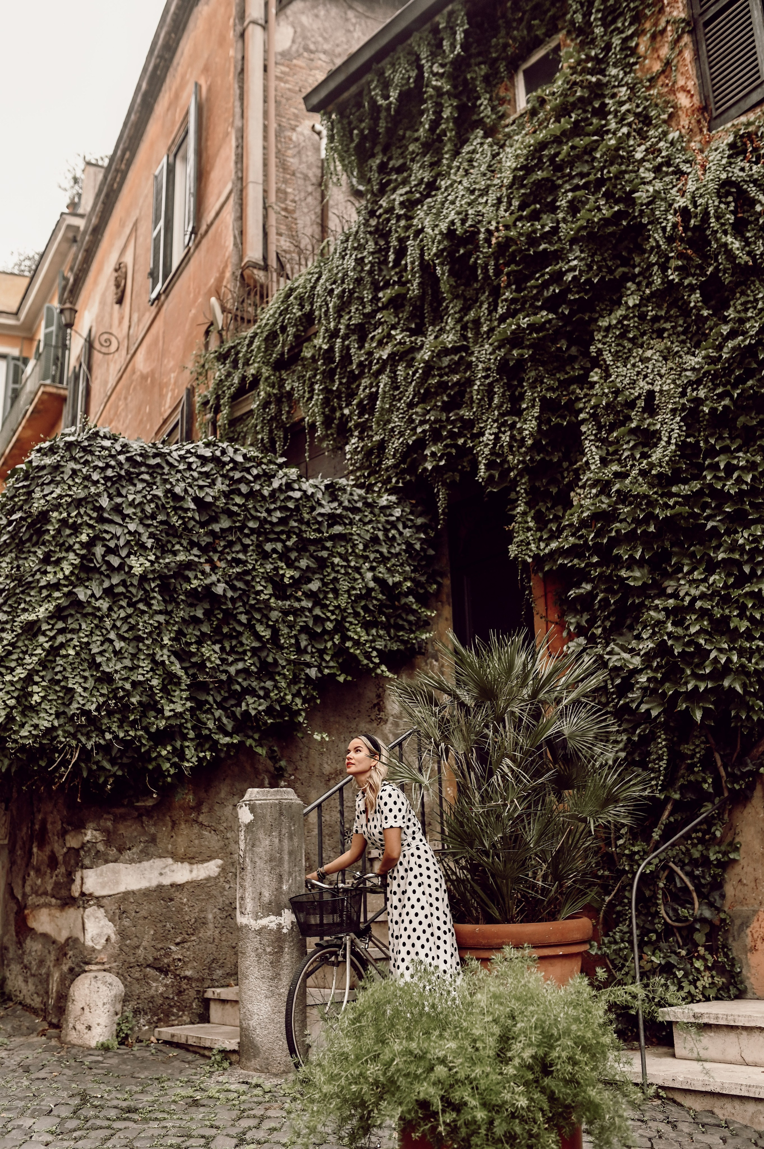 A woman in a polka-dot dress stands gracefully on stone steps in Trastevere, Rome.