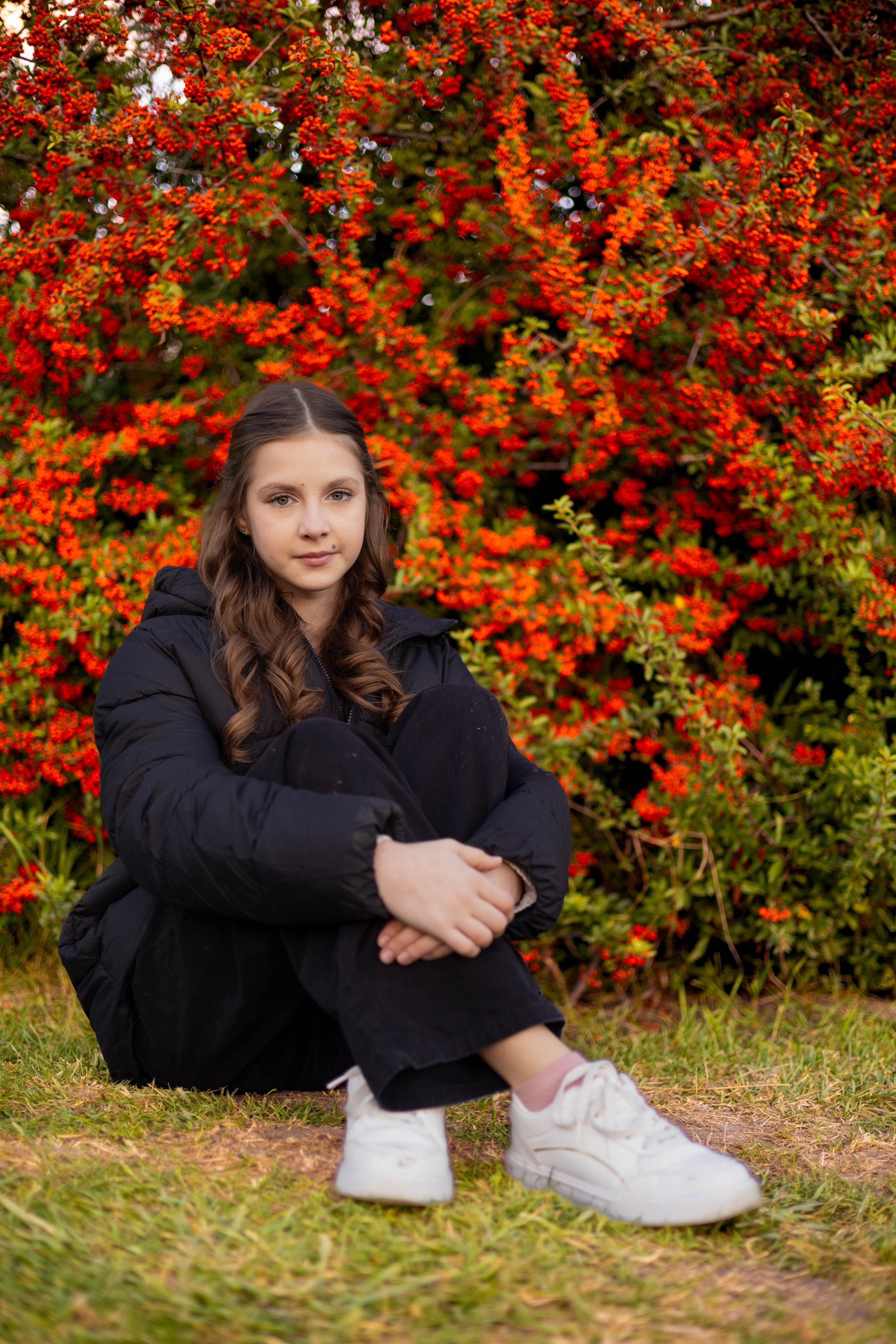 Девушка позирует на фоне куста с красными ягодами во время осенней фотосессии.