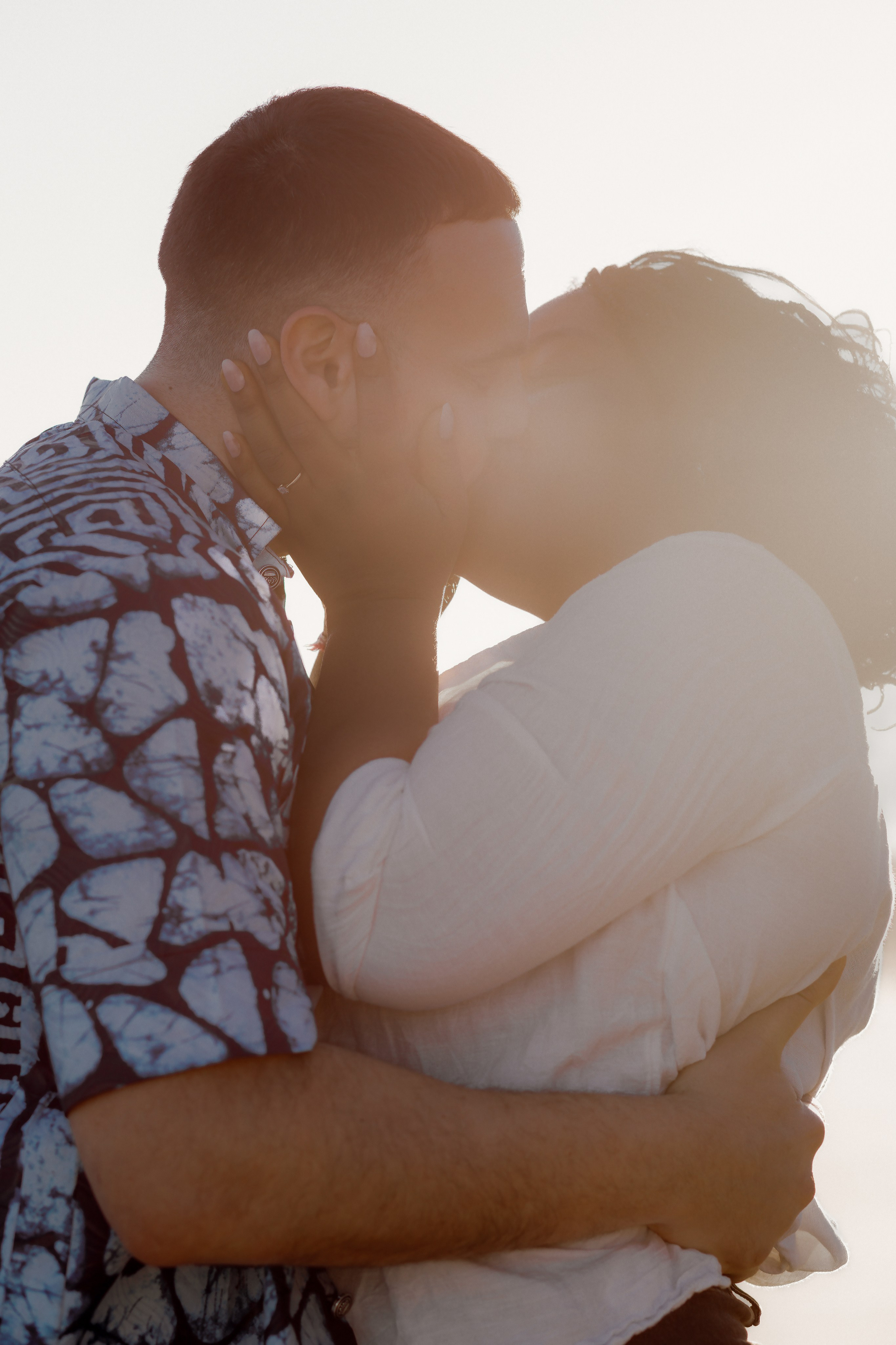 Primer plano romántico de una pareja compartiendo un beso durante una sesión de fotos en la playa al atardecer en Valencia, España — perfecto para quienes buscan sesiones auténticas y emocionales de historia de amor en Valencia y en toda España.