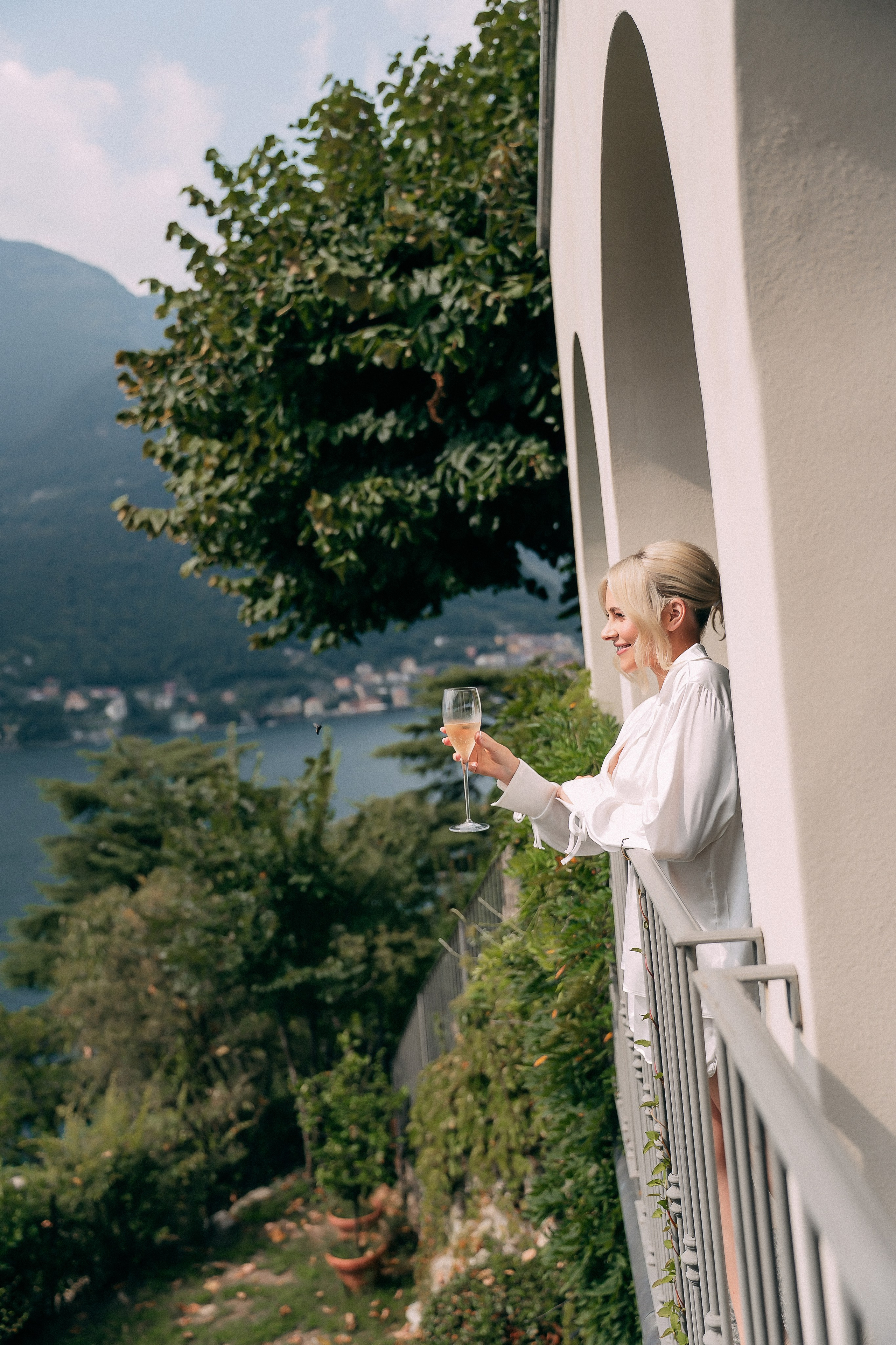 Bride in a robe overlooking Lake Como from a Villa Lario balcony, Italy