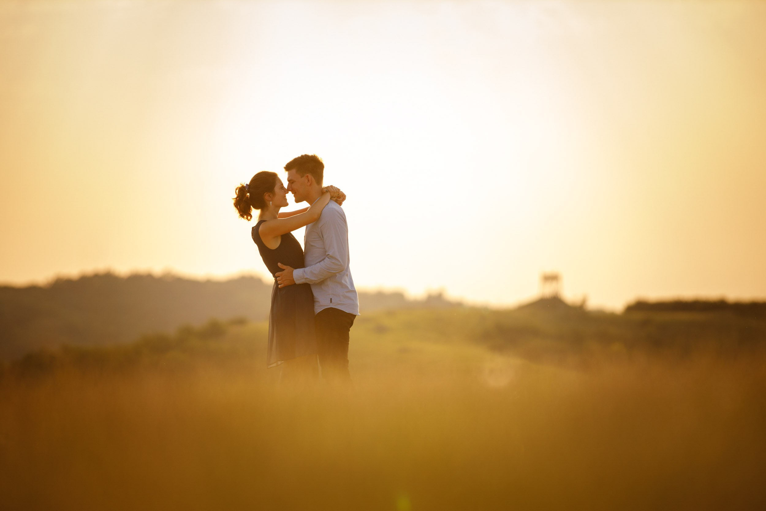 Zagrljaj mladenaca u polju tokom zalaska sunca, topla atmosfera i prirodno svetlo u wedding fotografiji.