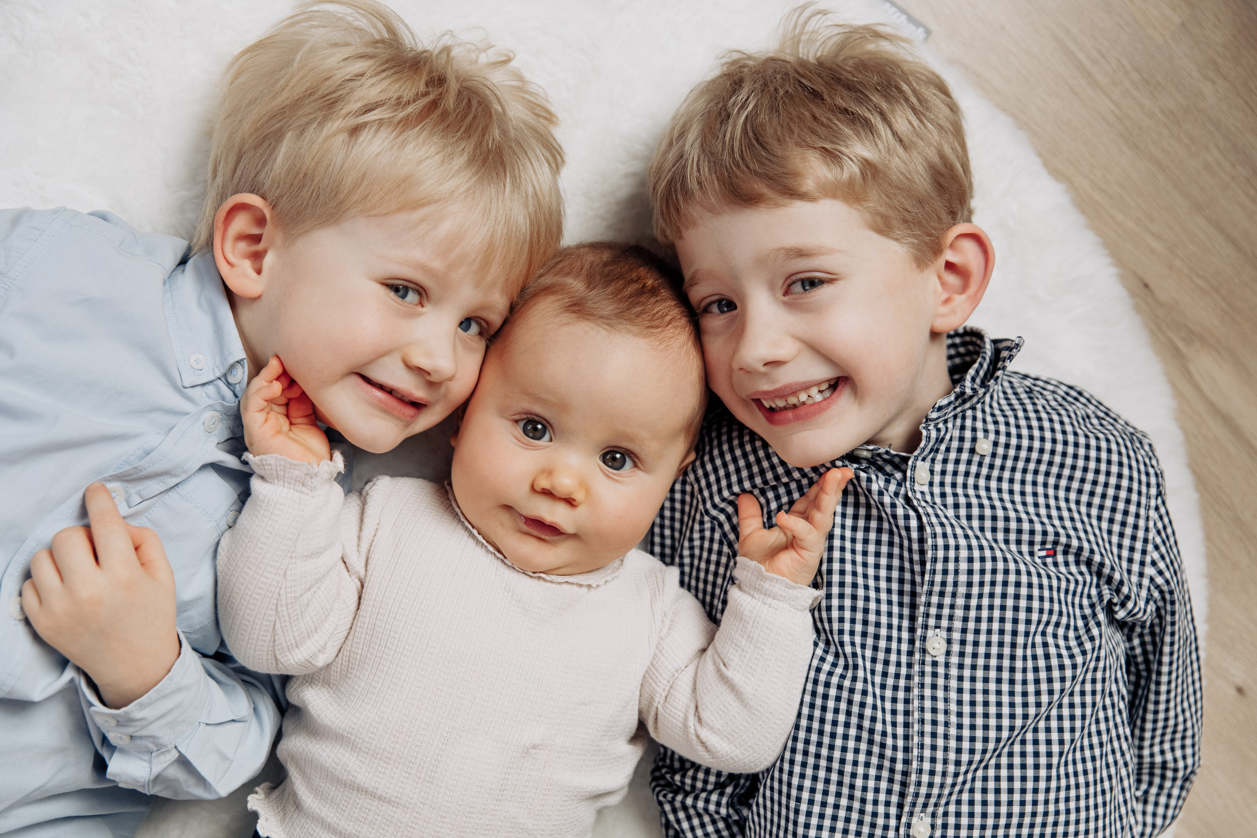 Zwei große Brüder liegen mit ihrer kleinen Schwester zusammen und lächeln glücklich.