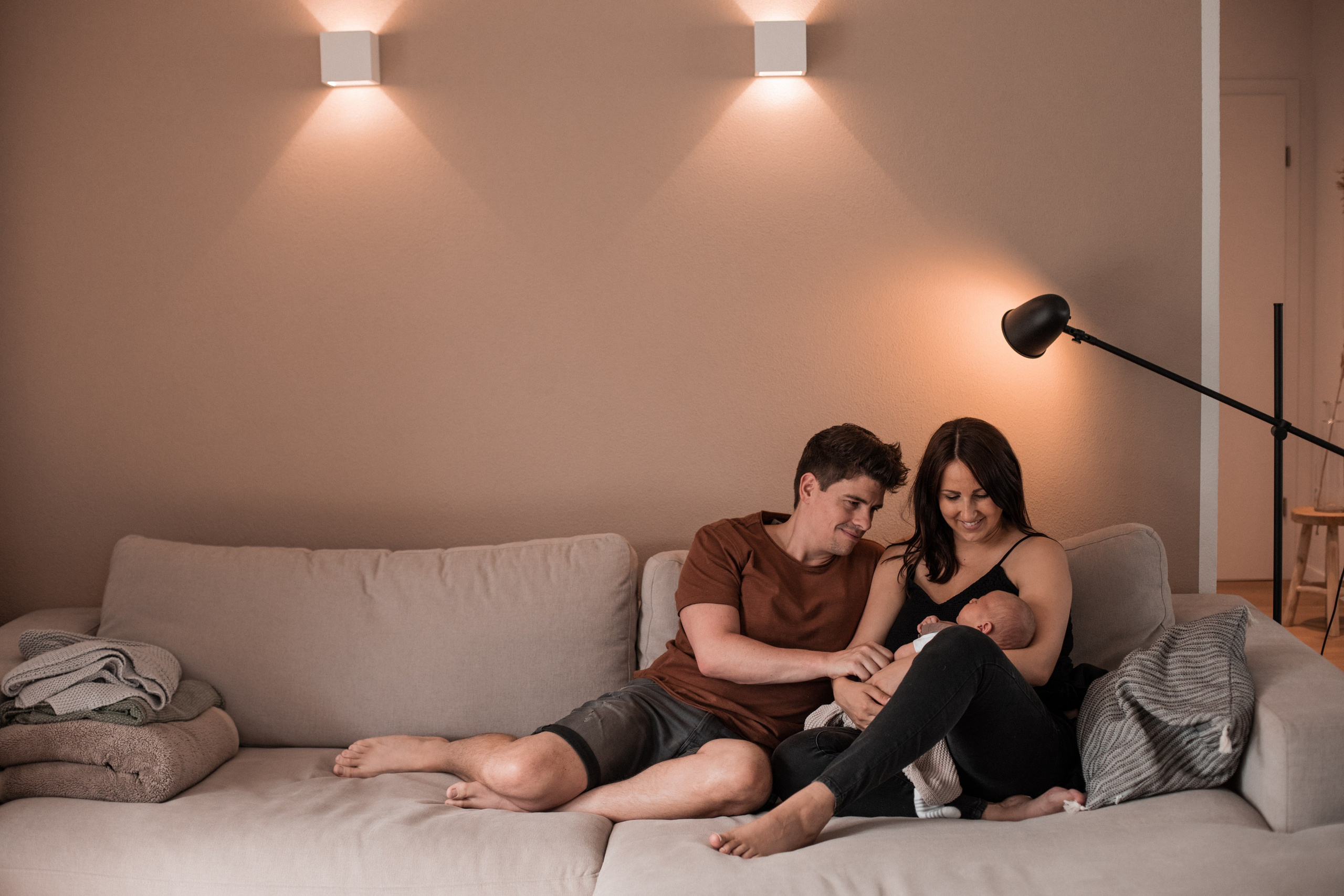 Mama und Papa sitzen auf dem Sofa, umarmen sich und bewundern ihr Neugeborenes zu Hause.