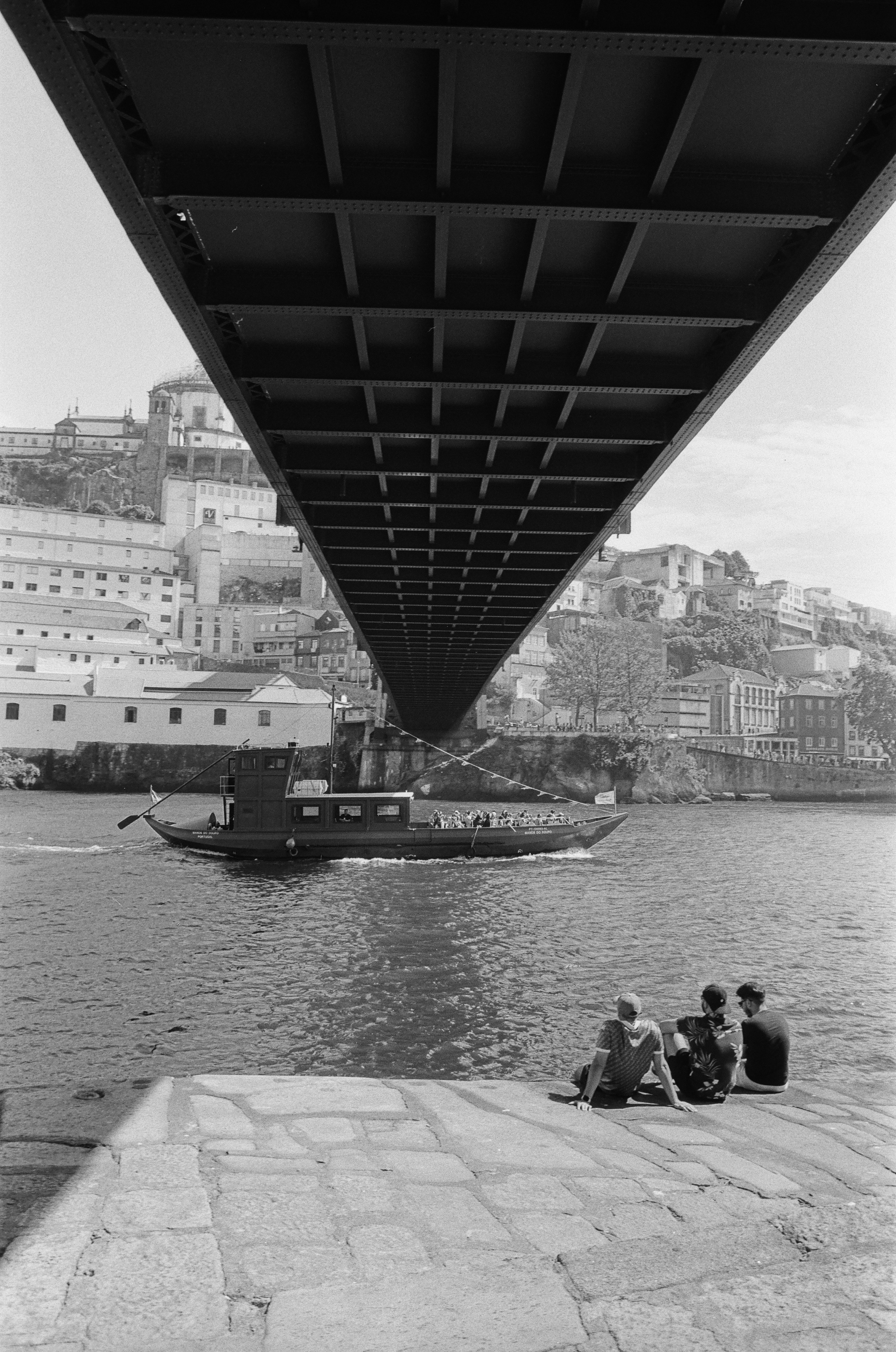 Blick unter die Ponte Dom Luís I mit Boot und Menschen am Ufer