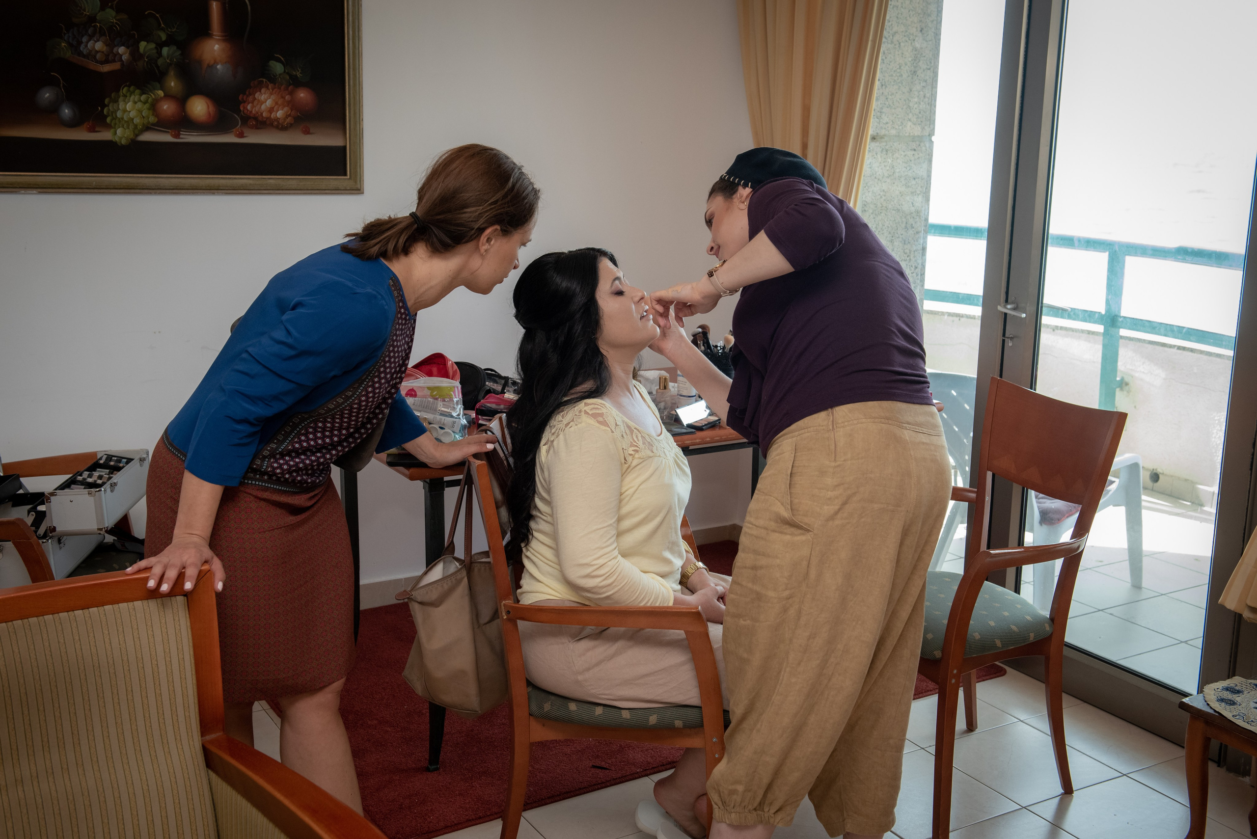 Bride getting her makeup done before the wedding, with two women assisting her. 