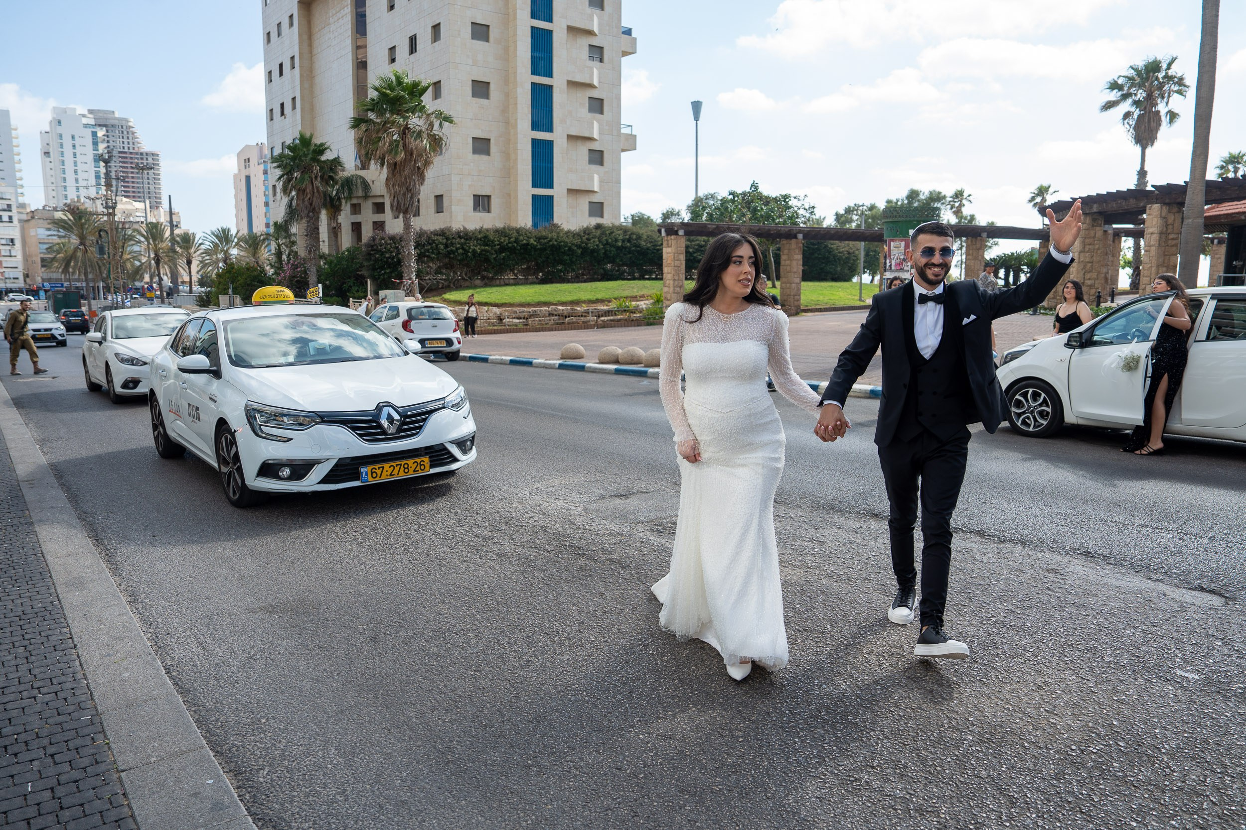 Bride Natali and groom Shimon walking hand in hand down a street in Netanya, Israel