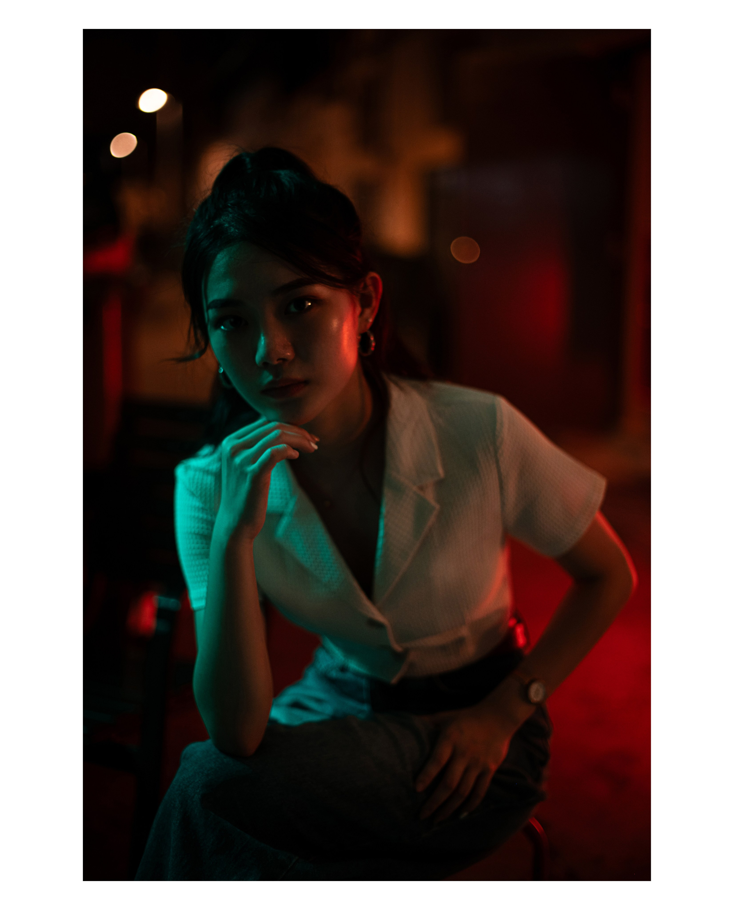 Moody and cinematic portrait of a young woman in Singapore's vibrant night setting, illuminated by contrasting neon teal and deep red hues. Captured by Singapore-based freelance photographer, specializing in fashion and creative portraiture, ideal for editorial projects, brand collaborations, and visual storytelling.