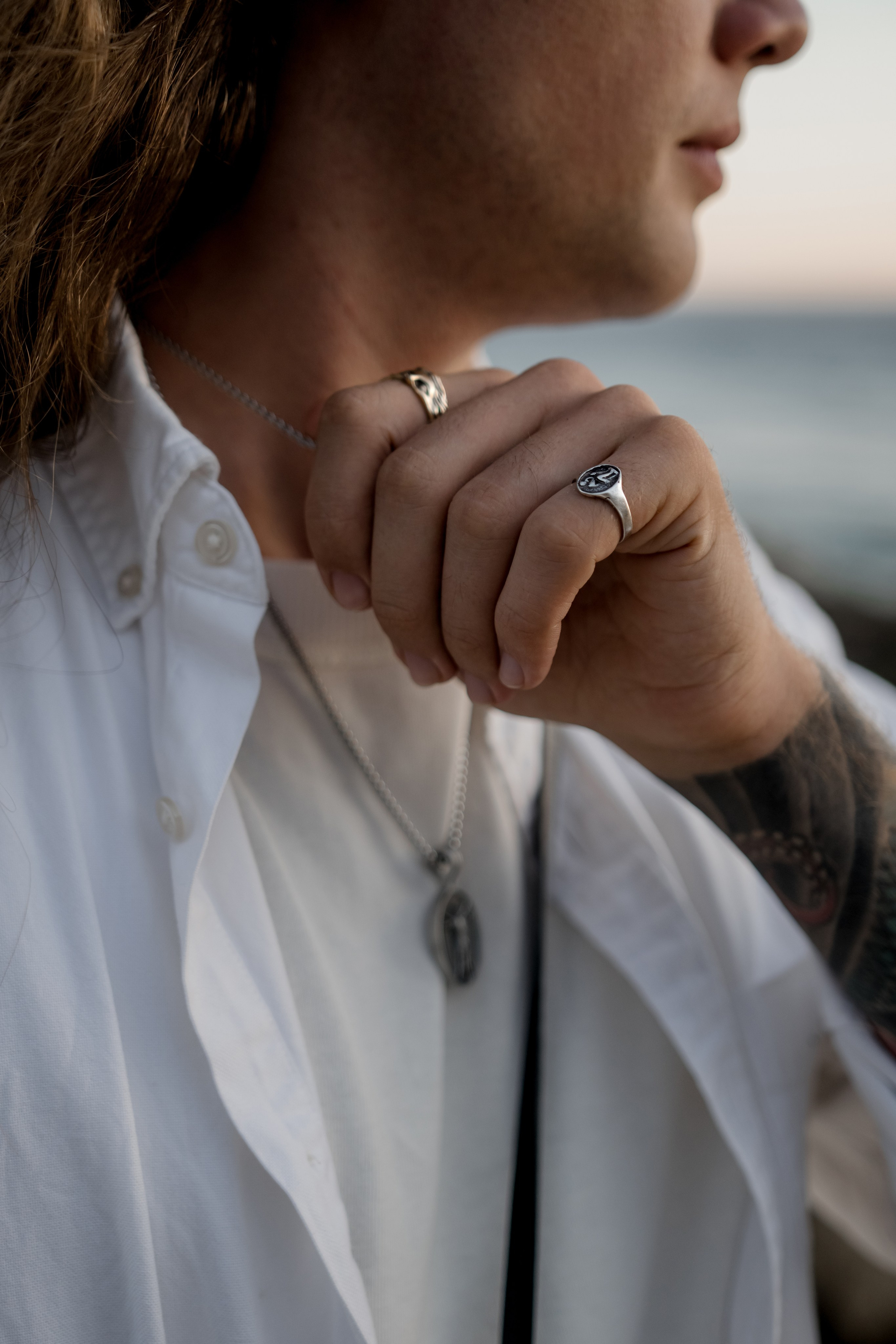 Close-up of a tattooed hand adjusting a bold silver ring, showcasing intricate accessory design.