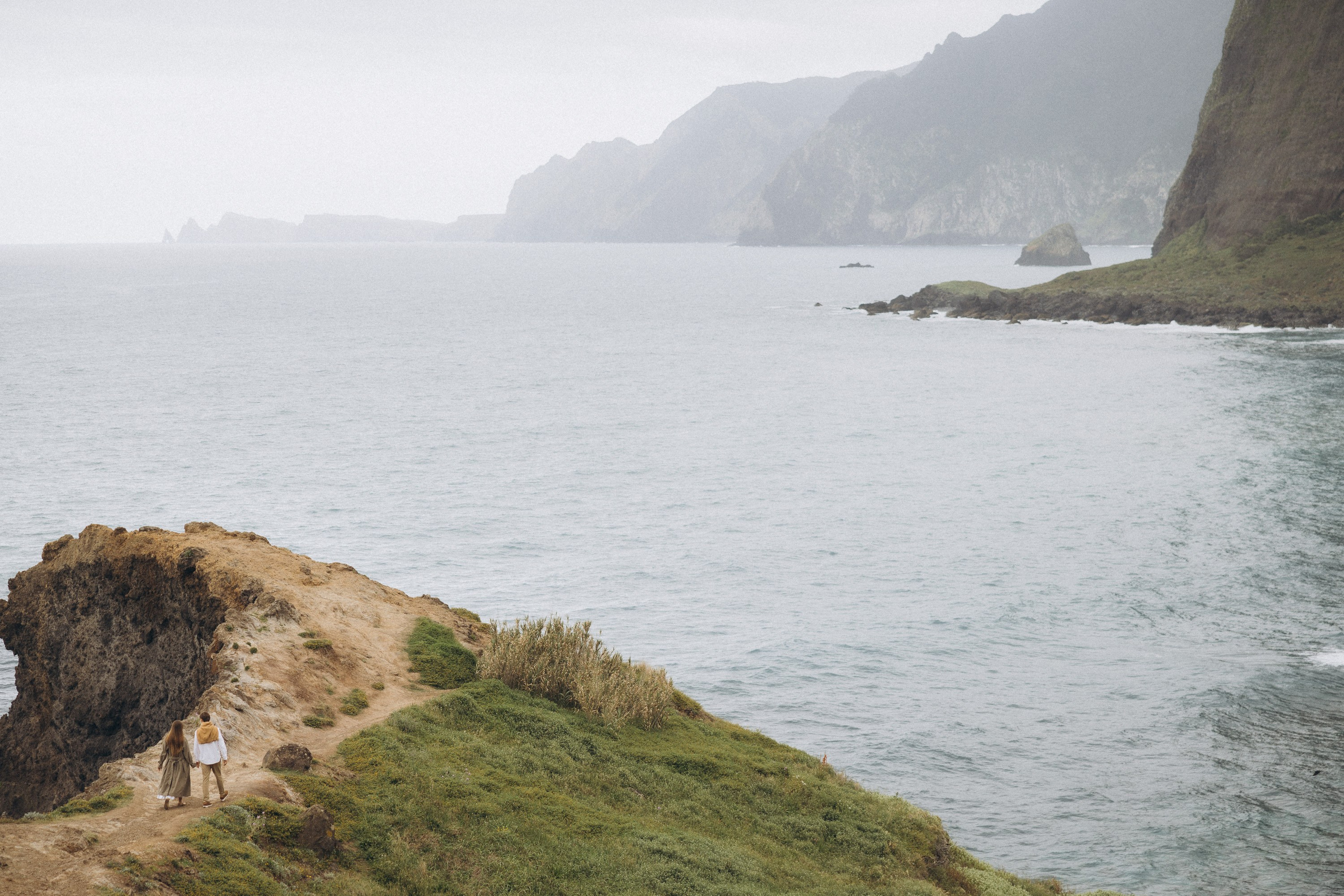 Beautiful engagement moment by the ocean in Madeira, Portugal, as one partner kneels to propose while waves crash in the background
