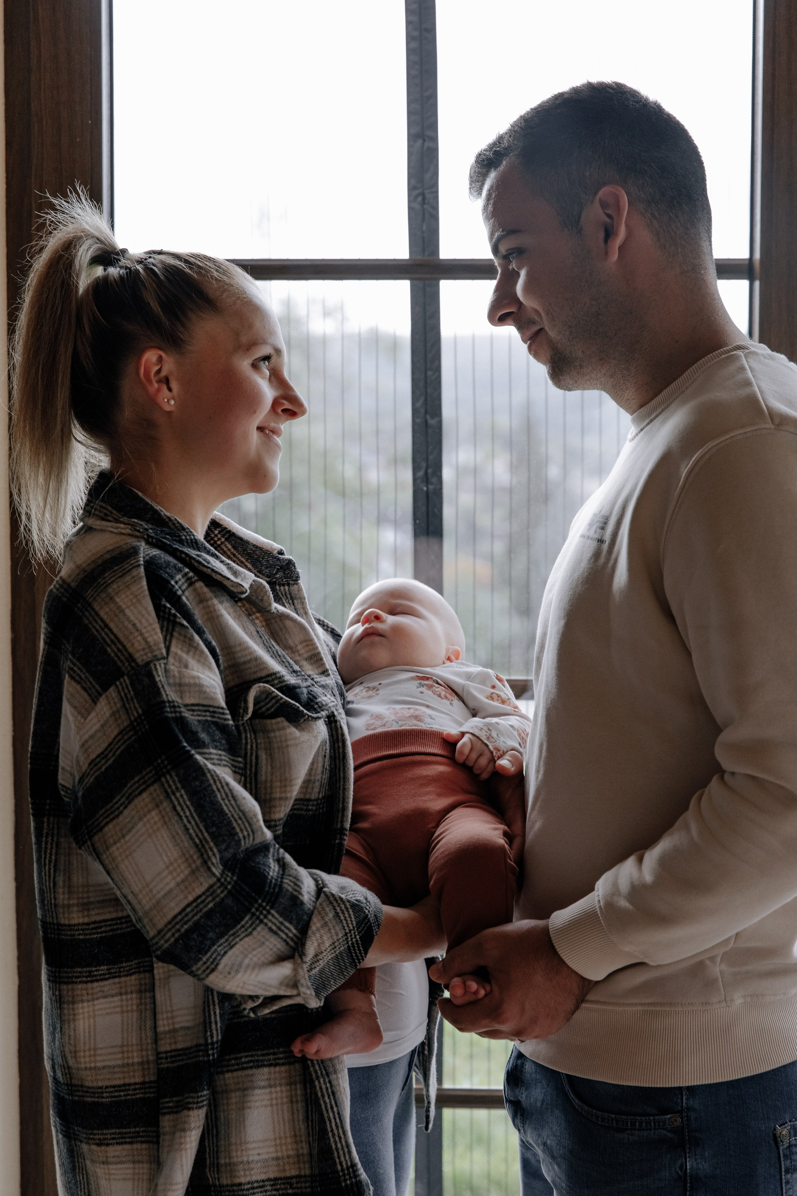 Mama und Papa stehen am Fenster und schauen sich liebevoll in die Augen.