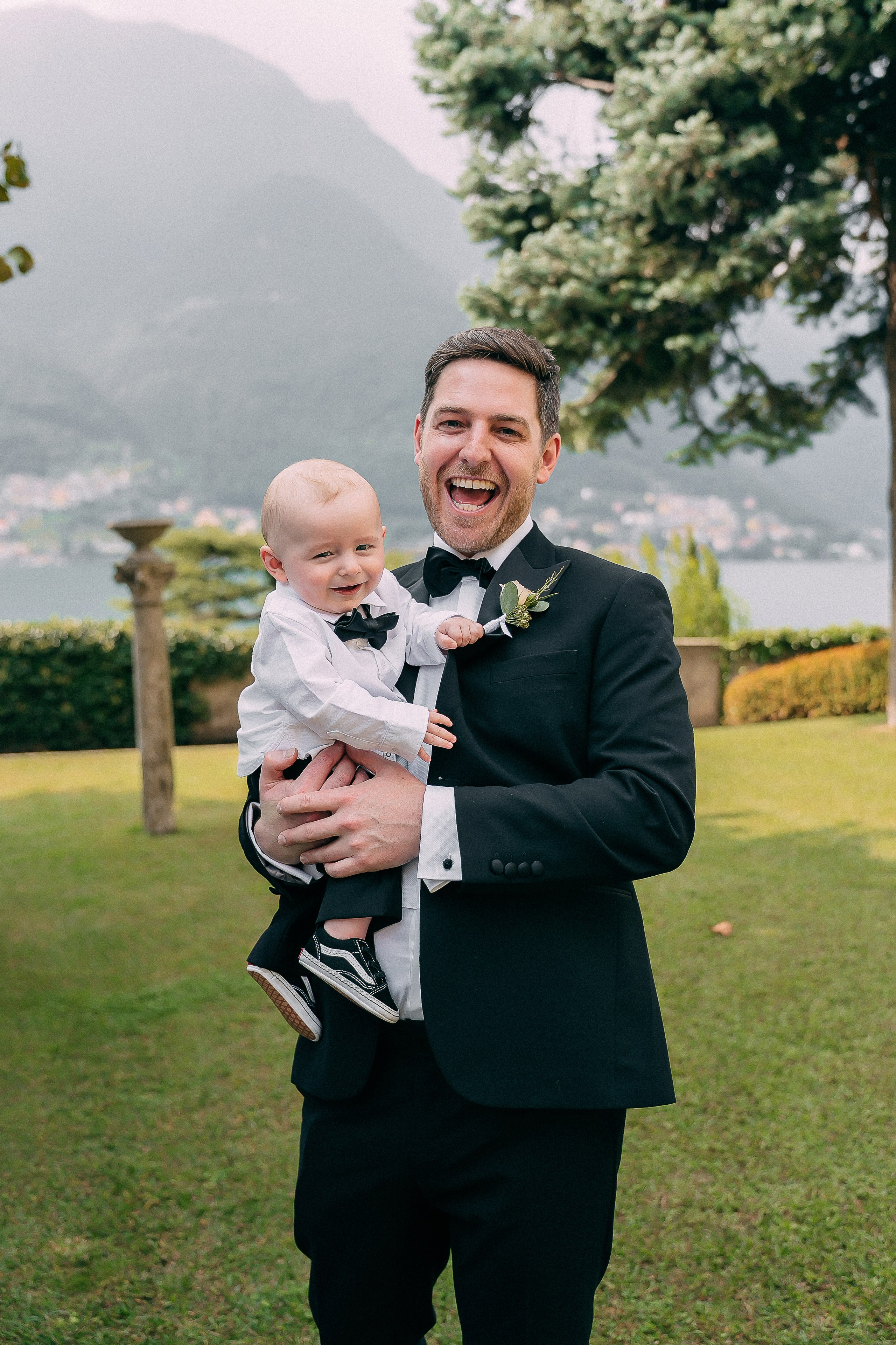 Groom holding a baby outdoors at Villa Lario, Lake Como, Italy