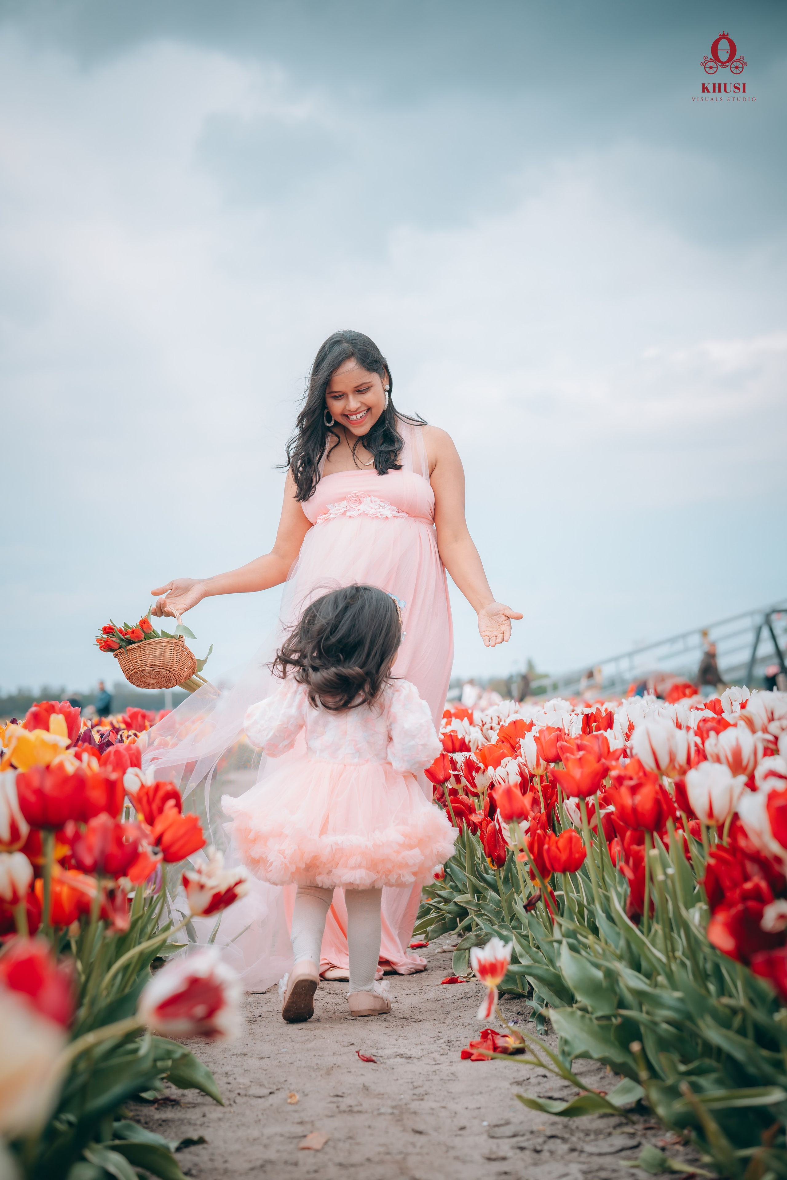 A daughter running towards her mother holding a tulip flower basket in a white red tulip flower field in Netherlands