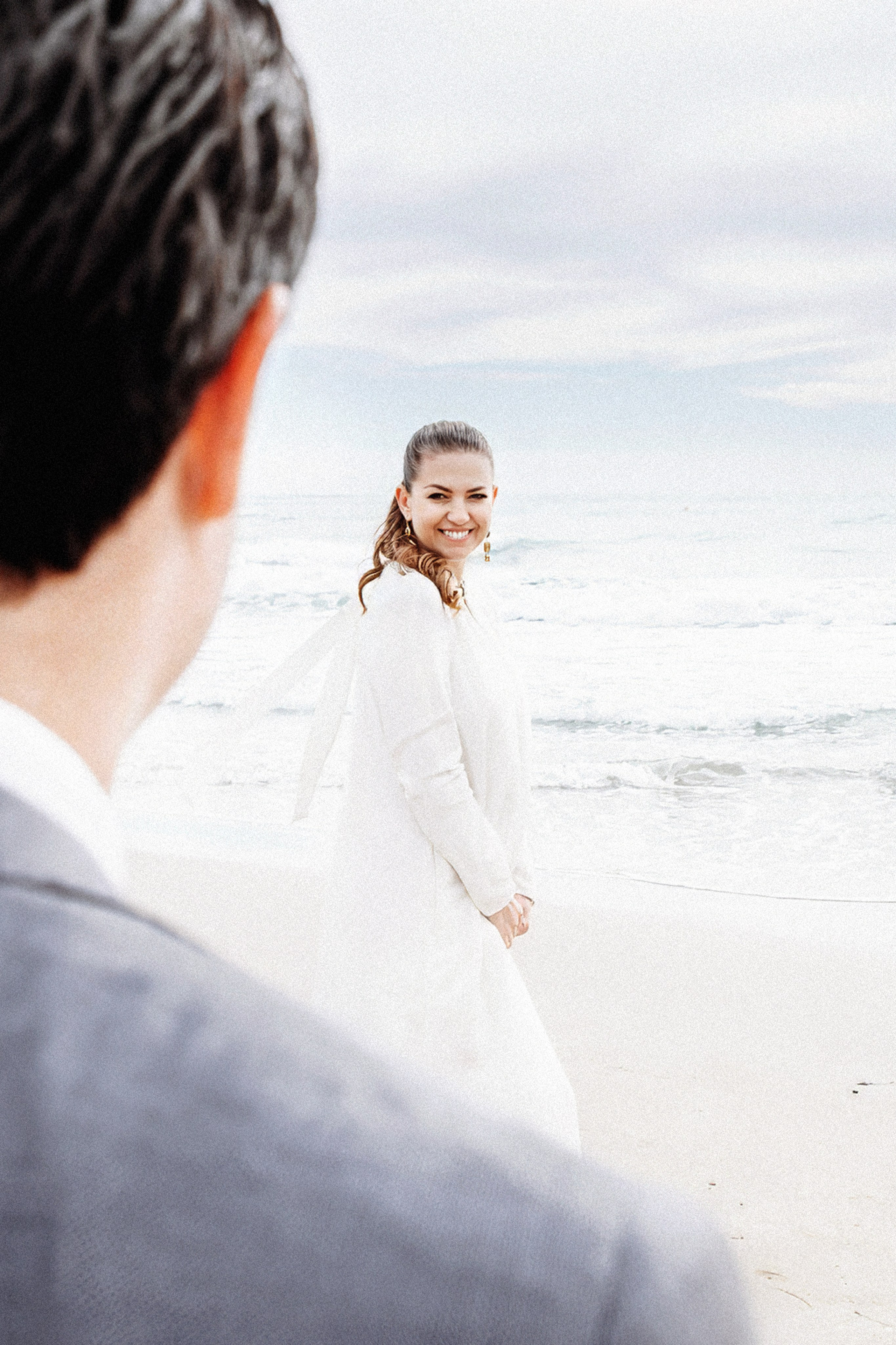Bride smiling at her groom by the sea in València, Spain, captured in a natural, candid destination wedding photography style with soft coastal light.