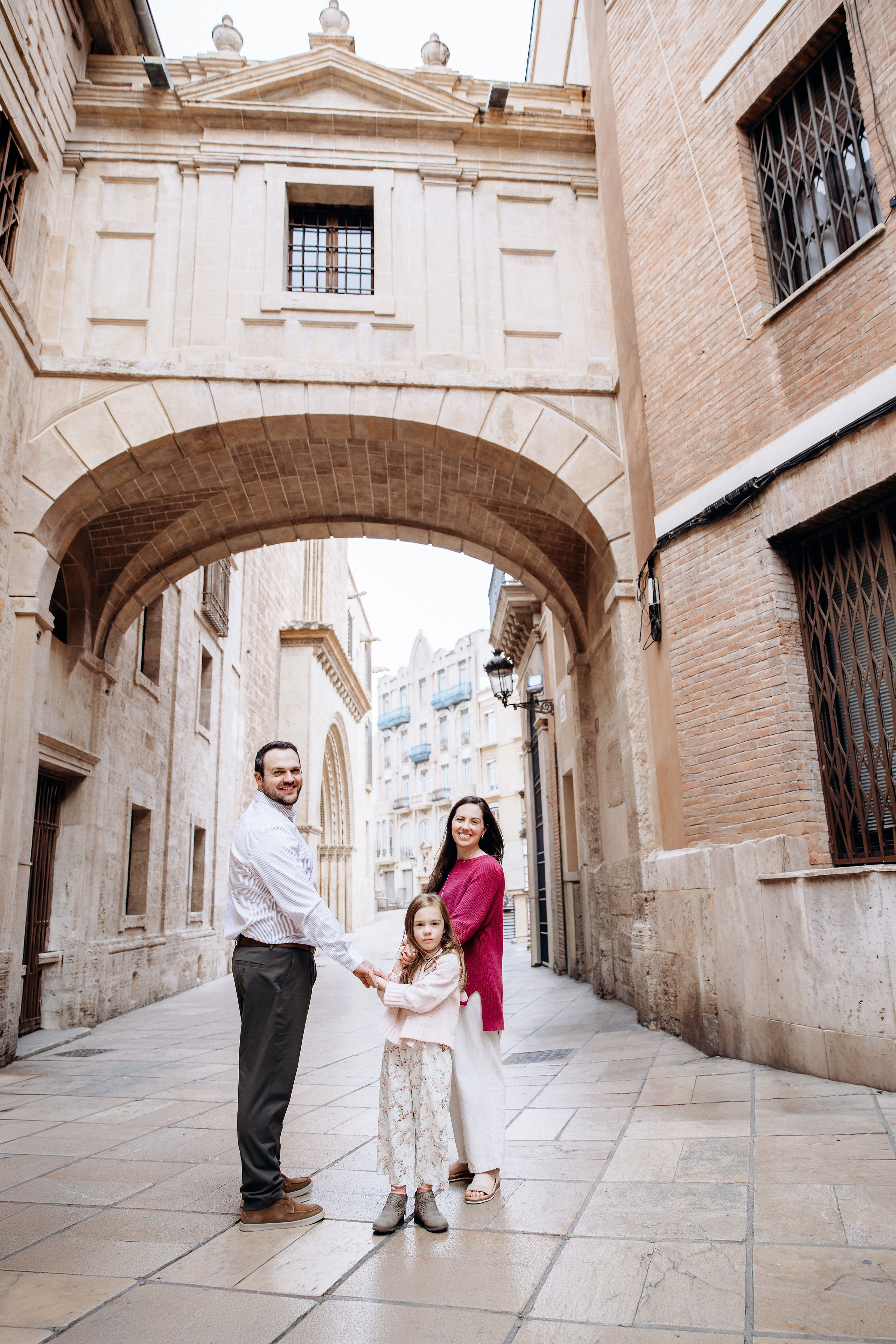 Семейная фотосессия в Валенсии, Испания, где отец и ребёнок играют вместе под исторической каменной аркой в старом городе, снято при естественном свете для живого и радостного семейного момента — идеально для семейных фотосессий в Валенсии и по всей Испании.