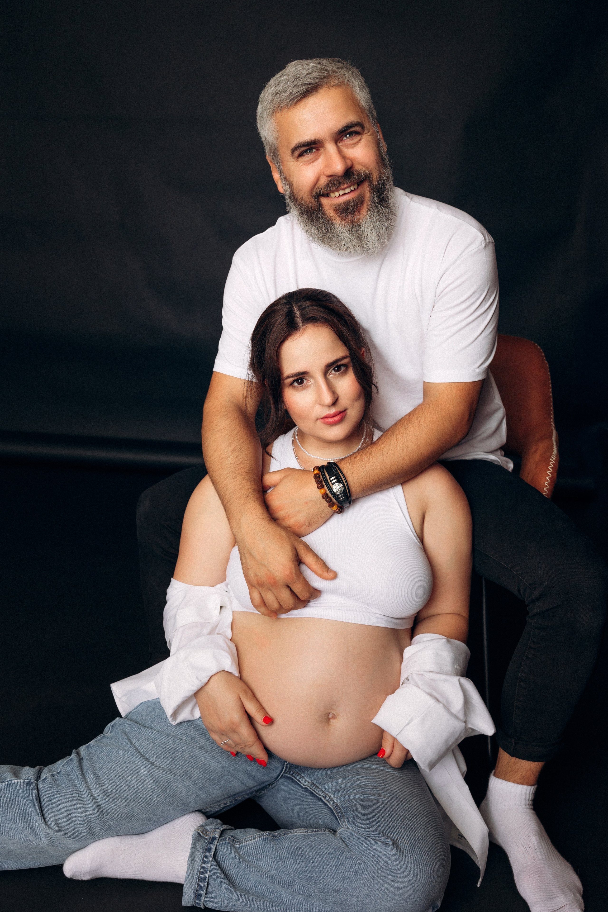 Ciepło i partnerstwo – przyszli rodzice siedzą na podłodze w objęciach, fotografia ciążowa pełna bliskości.