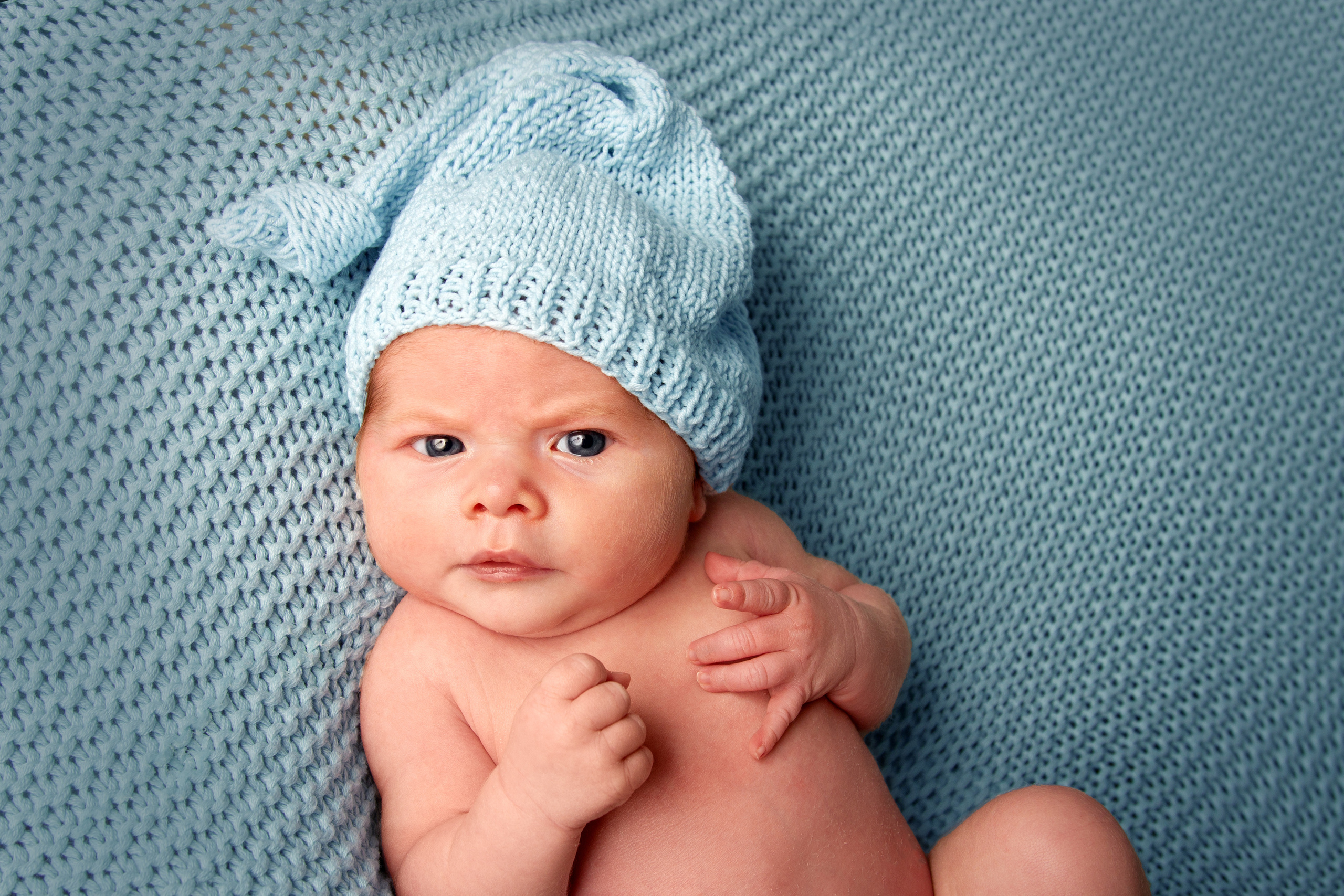 Ein Baby mit blauem  Haube liegt auf einer blauen Strickdecke