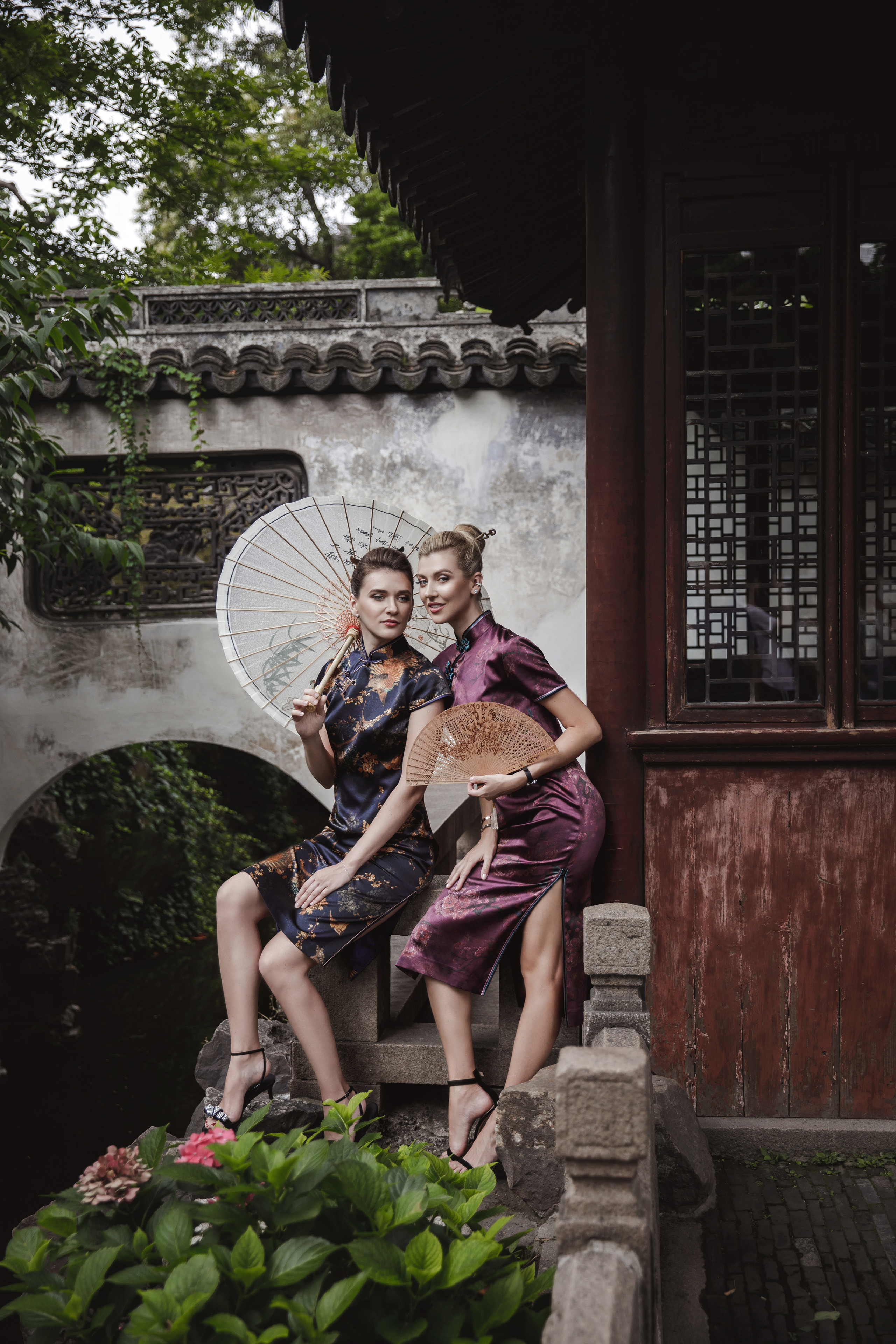 Two friends, sisters of European-looking girls in Chinese traditional dress, with Chinese umbrella in YuGarden, Shanghai, China.