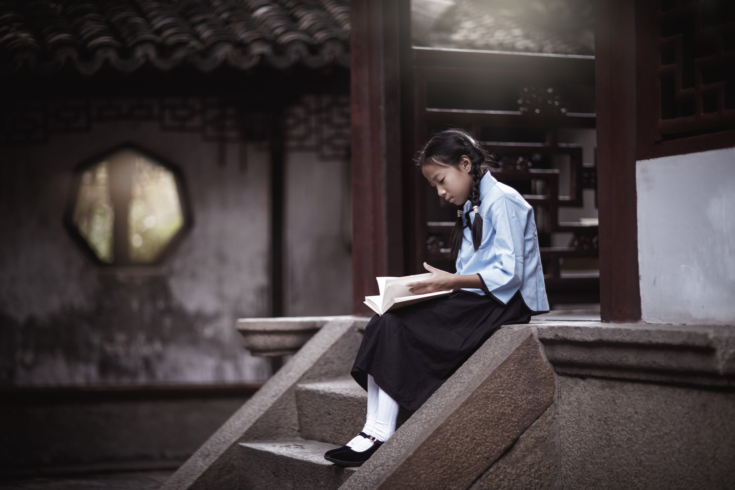 Atmospheric photo shoot in 1950s style in Shanghai. Pioneer girl in the Garden of Joy reading a book. 
