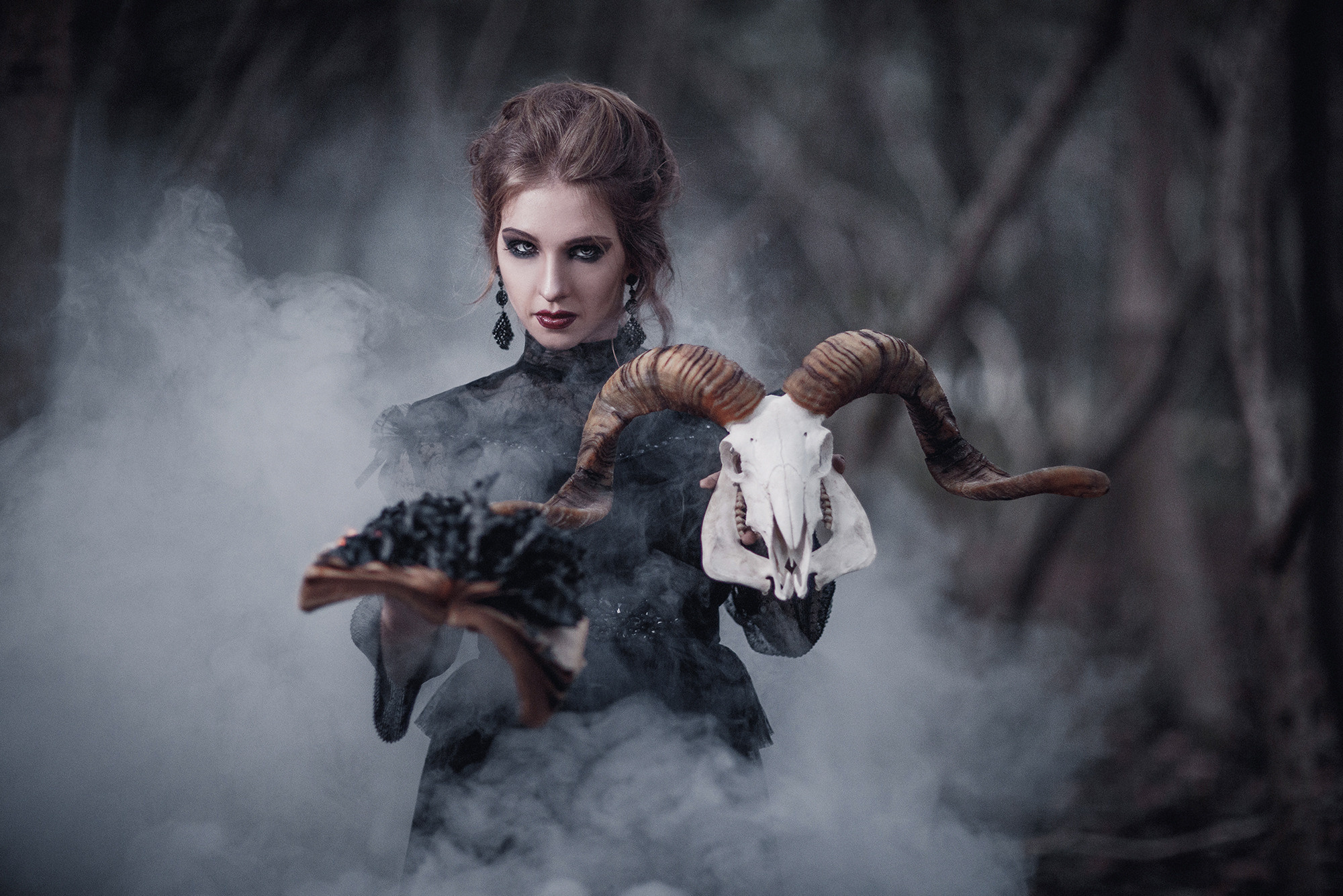 Artistic photo shoot. girl in the image of a witch, wearing a black chiffon dress with a large hood, in her hands she has a real mountain goat skull. Photo session in Shanghai park.