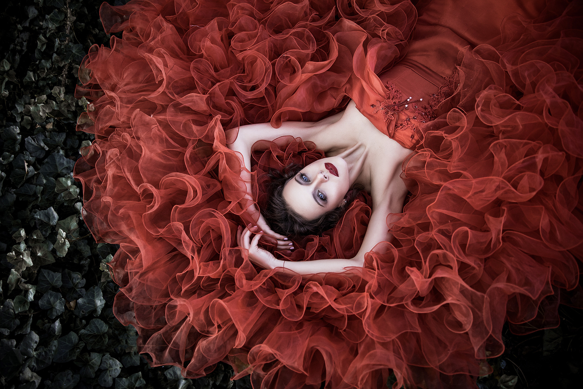 Girl in a lush red dress lying on the grass. Shooting in a park in Shanghai