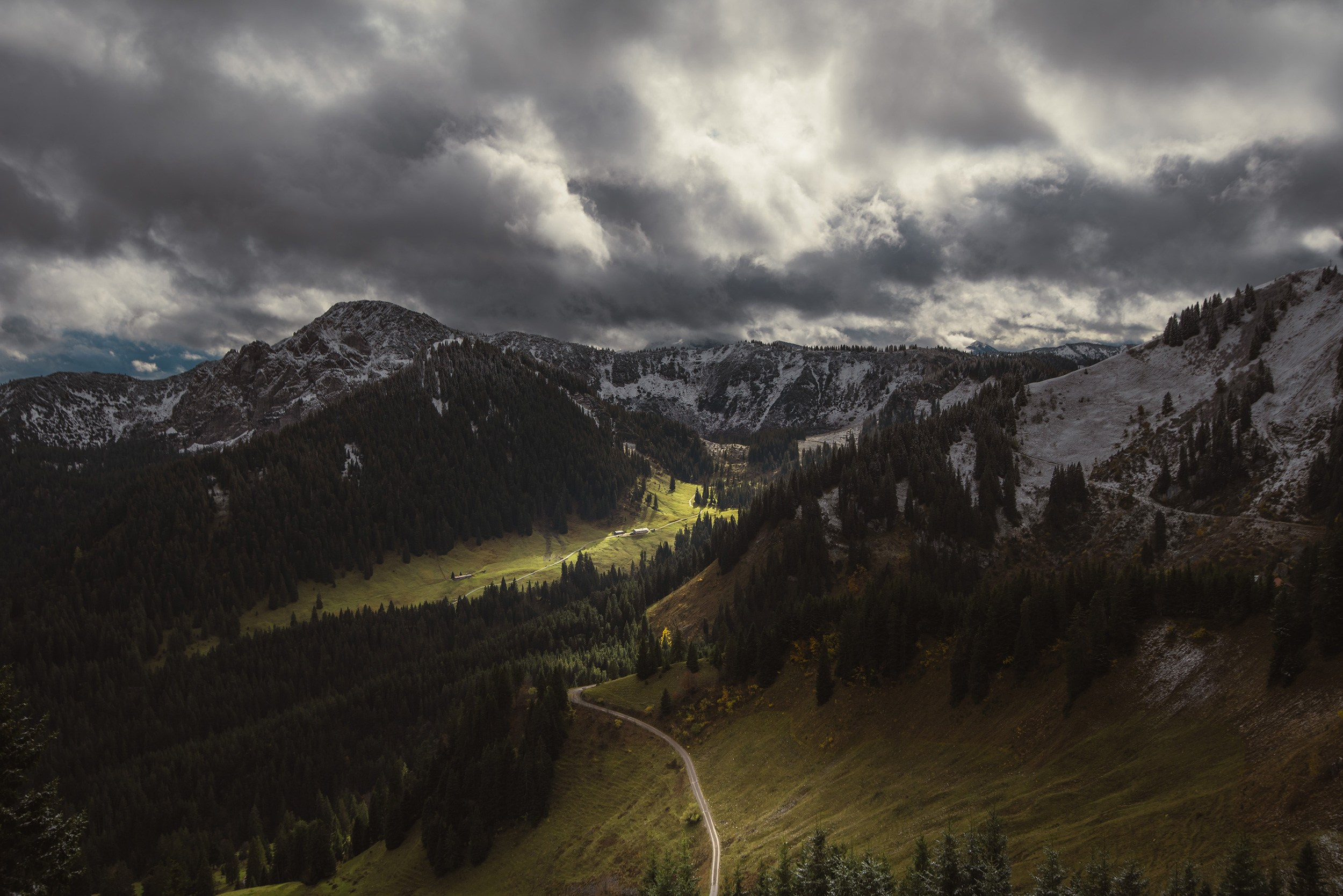 Green valley and trails of Mount Wallberg under a dramatic cloudy sky.