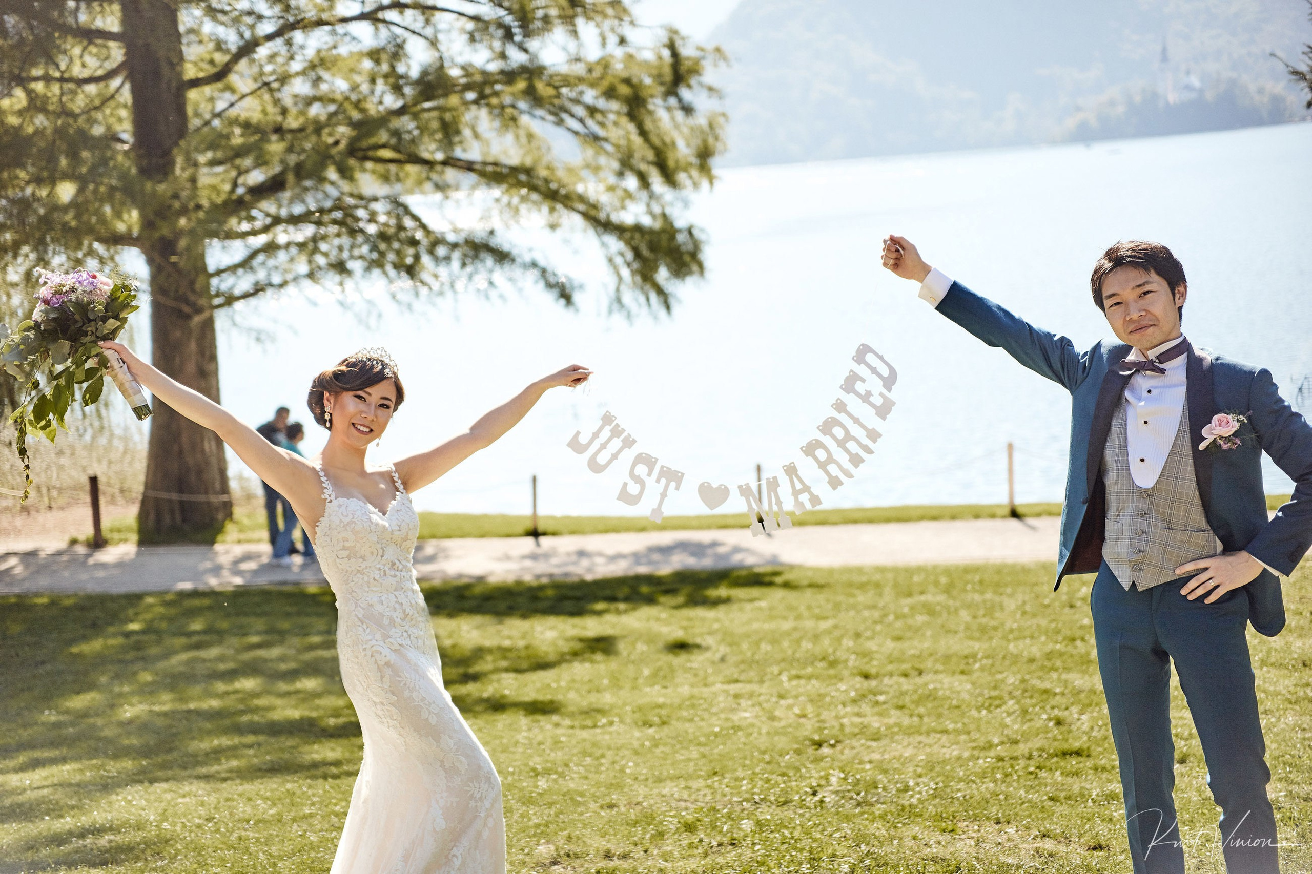 Jubilant Japanese newlyweds jumping through Heart of Bled installation.