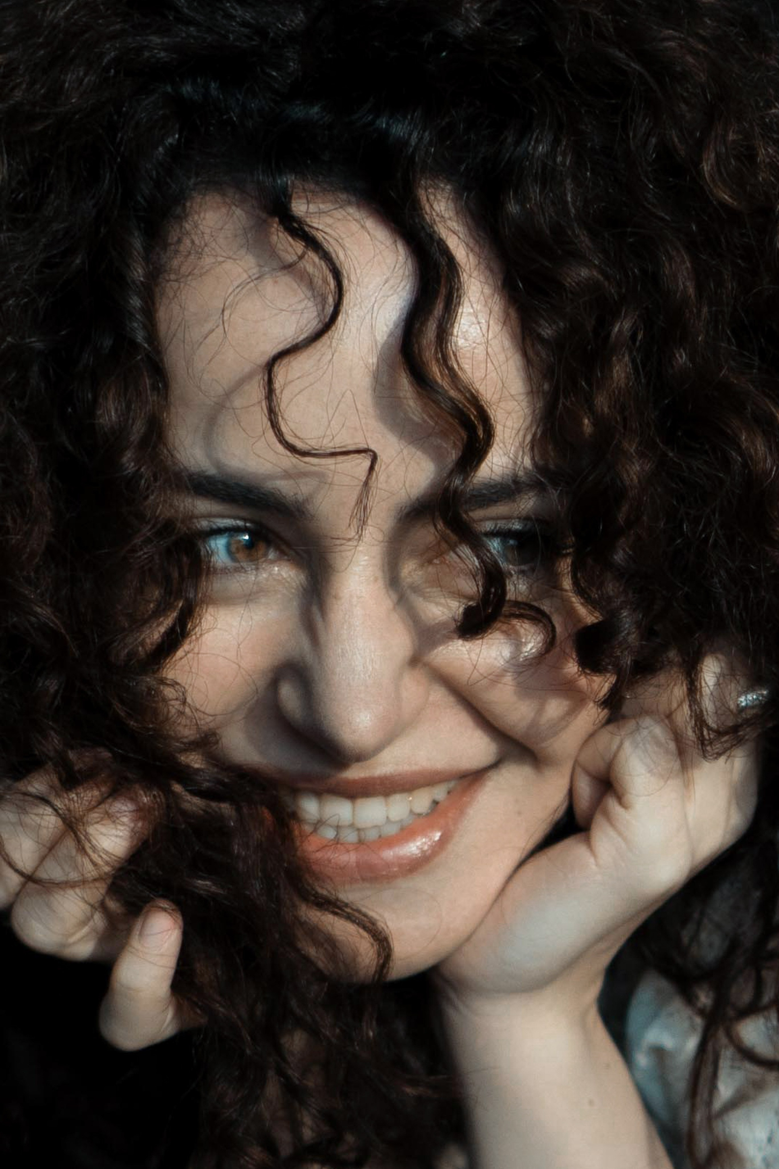 Lebendiges Portrait, Frau mit Locken lacht und stützt das Gesicht – künstlerisches Frauenportrait