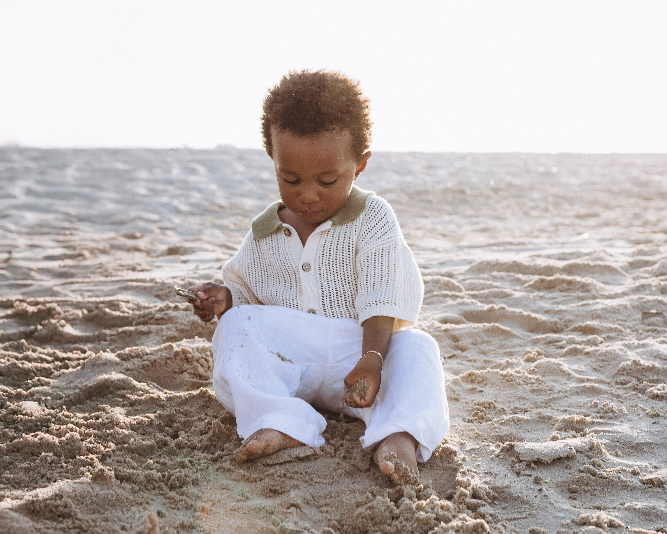 Adorable niño pequeño jugando con arena en la playa de Alicante, España — momento espontáneo que captura la curiosidad infantil durante una sesión familiar al atardecer junto al mar.